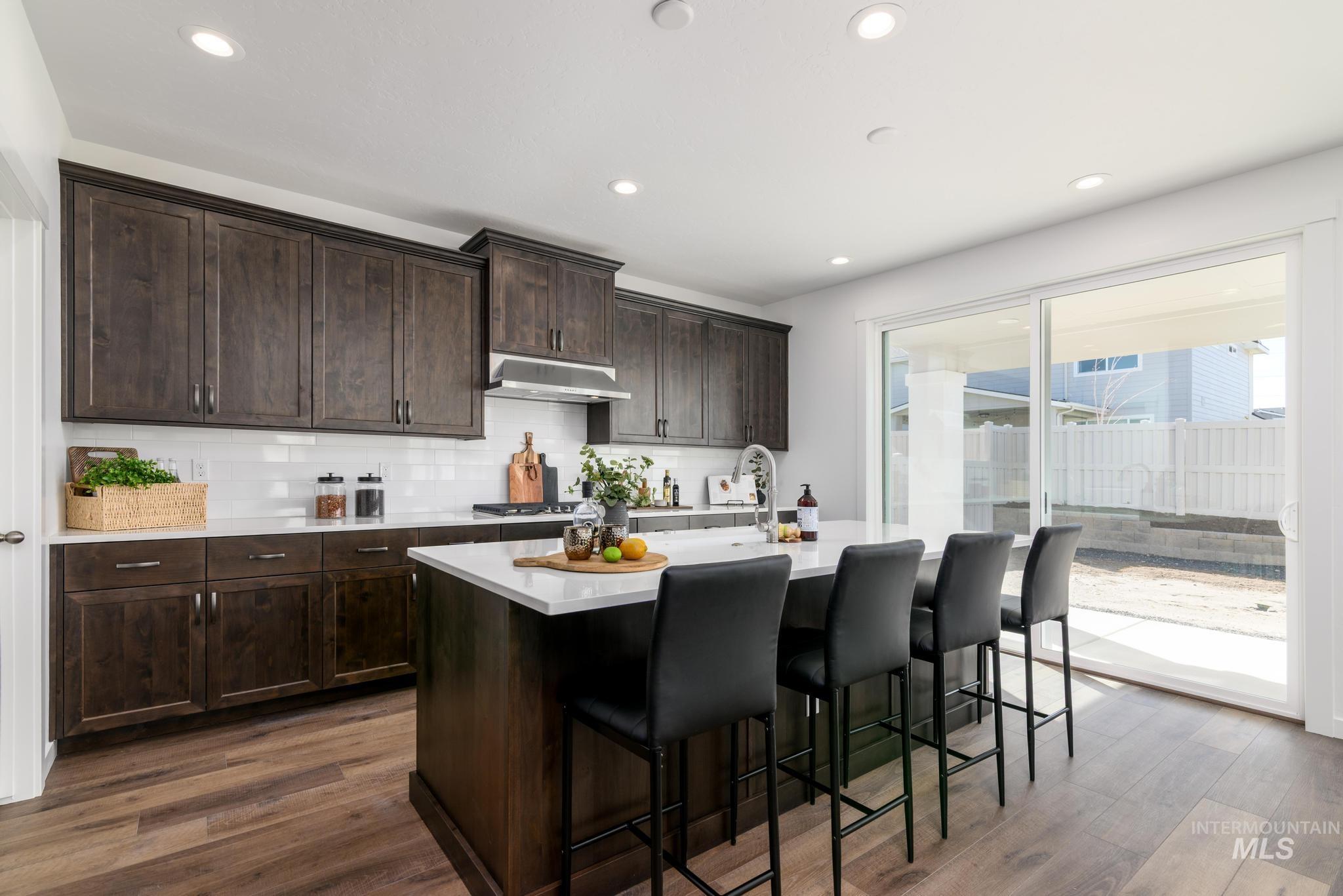 Kitchen featuring dark brown cabinets, dark wood-style floors, an island with sink, a kitchen bar, and recessed lighting