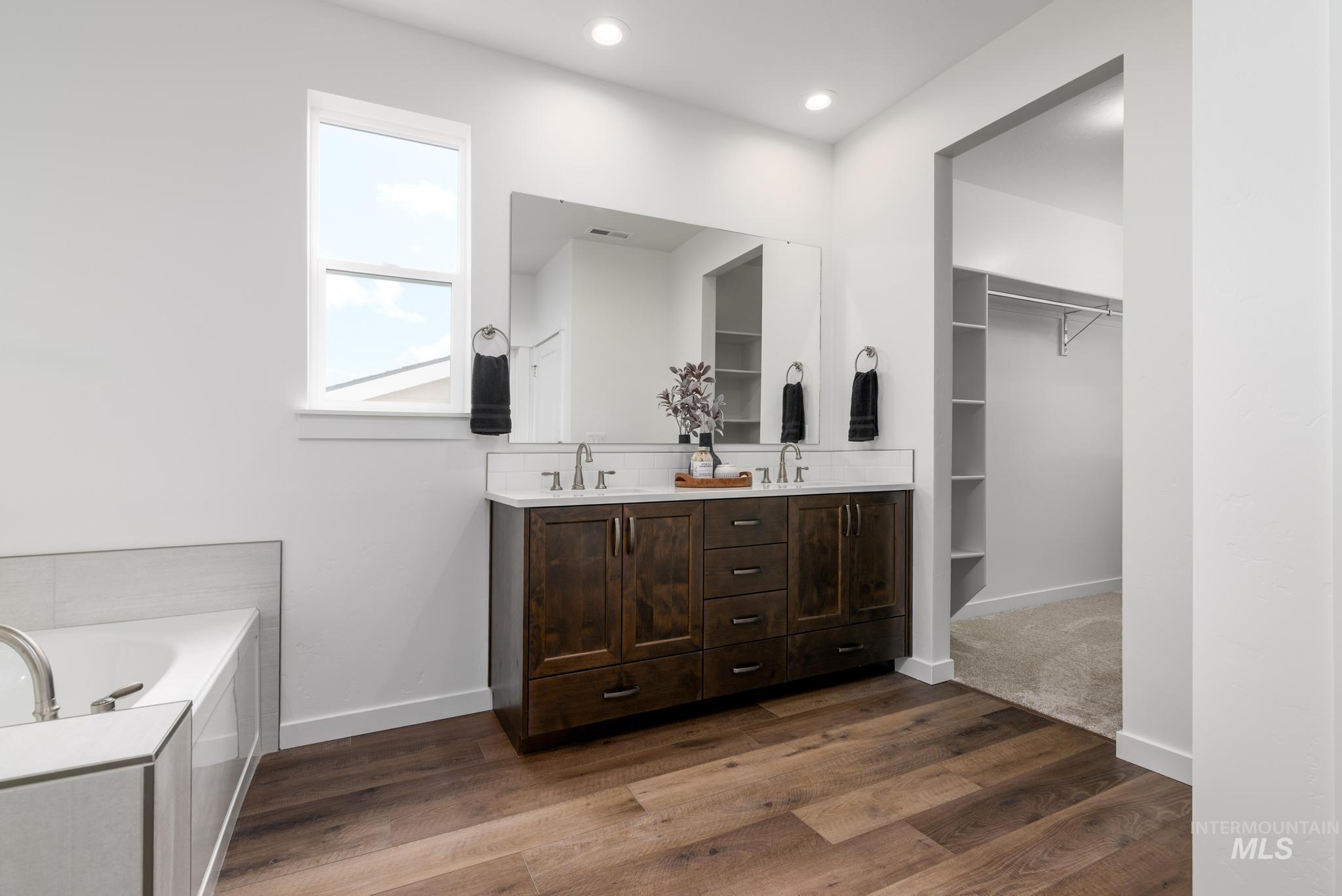 Bathroom featuring double vanity, a garden tub, dark wood-type flooring, a spacious closet, and recessed lighting