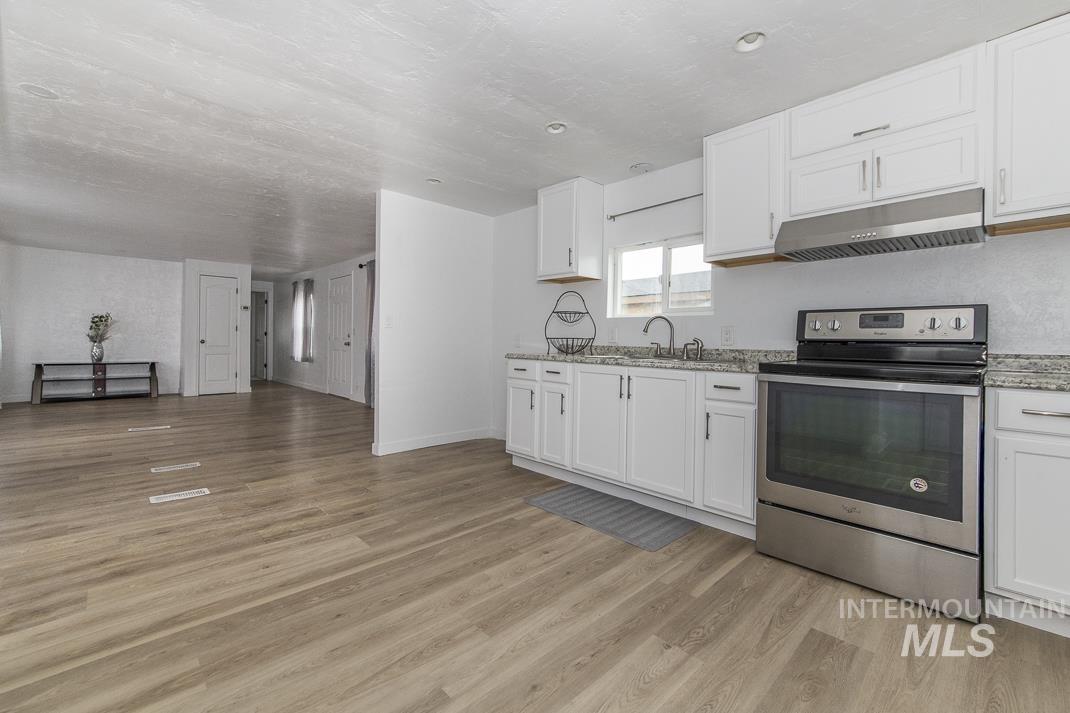 Kitchen featuring electric stove, white cabinetry, under cabinet range hood, and light stone countertops