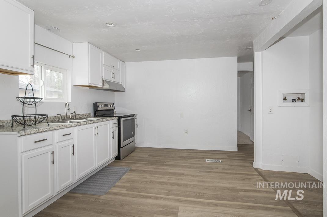 Kitchen featuring stainless steel electric stove, white cabinets, light wood finished floors, light stone countertops, and under cabinet range hood
