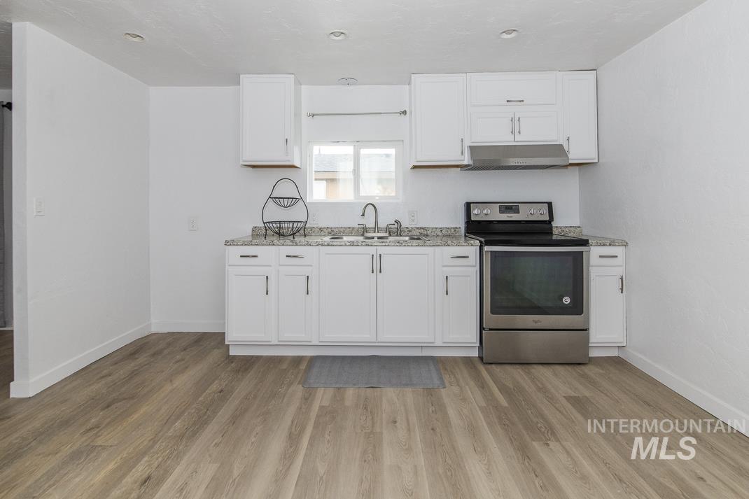 Kitchen featuring stainless steel range with electric stovetop, white cabinets, under cabinet range hood, light stone counters, and light wood-style flooring