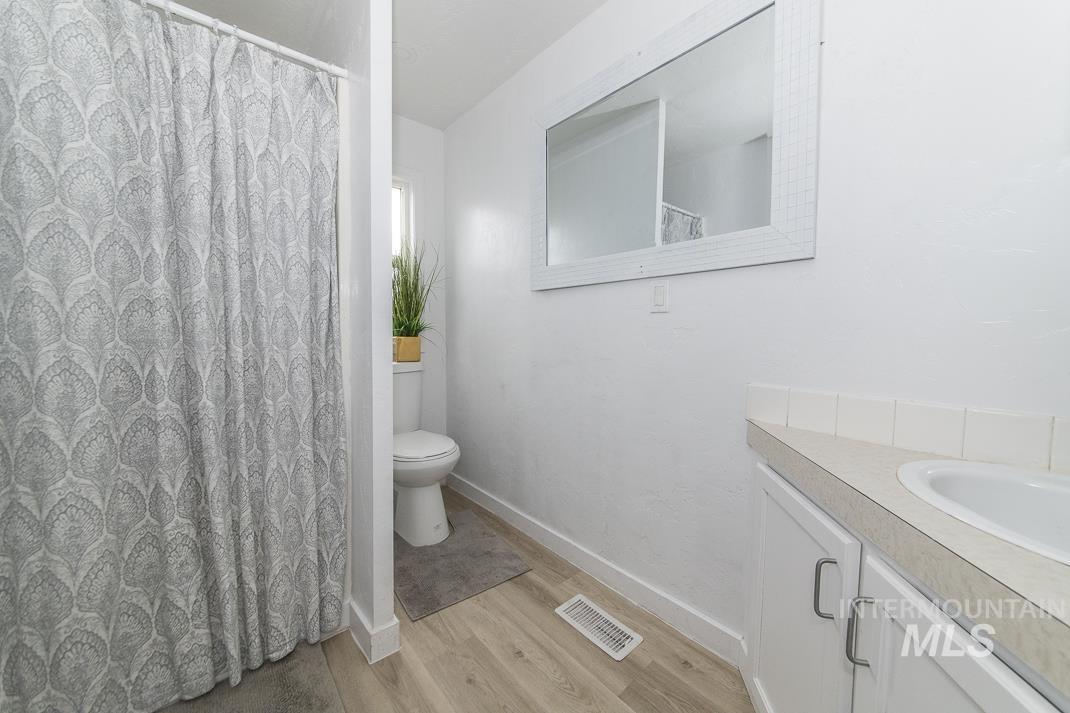 Full bath with curtained shower, vanity, and light wood-style floors