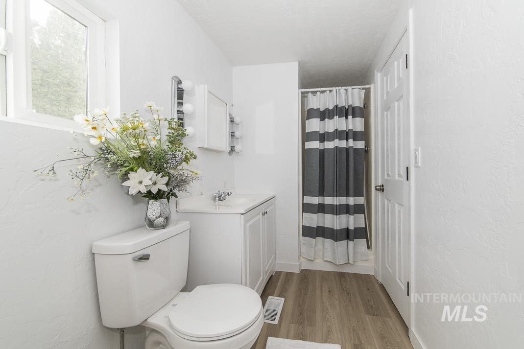 Full bath featuring curtained shower, vanity, light wood-style floors, and a textured wall