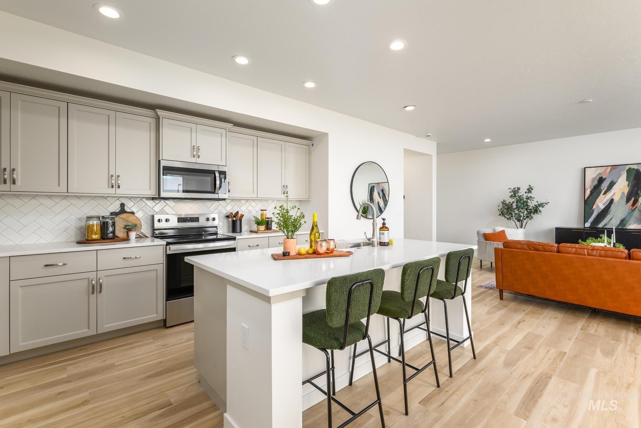 Kitchen featuring appliances with stainless steel finishes, a center island with sink, backsplash, a breakfast bar, and light wood-type flooring