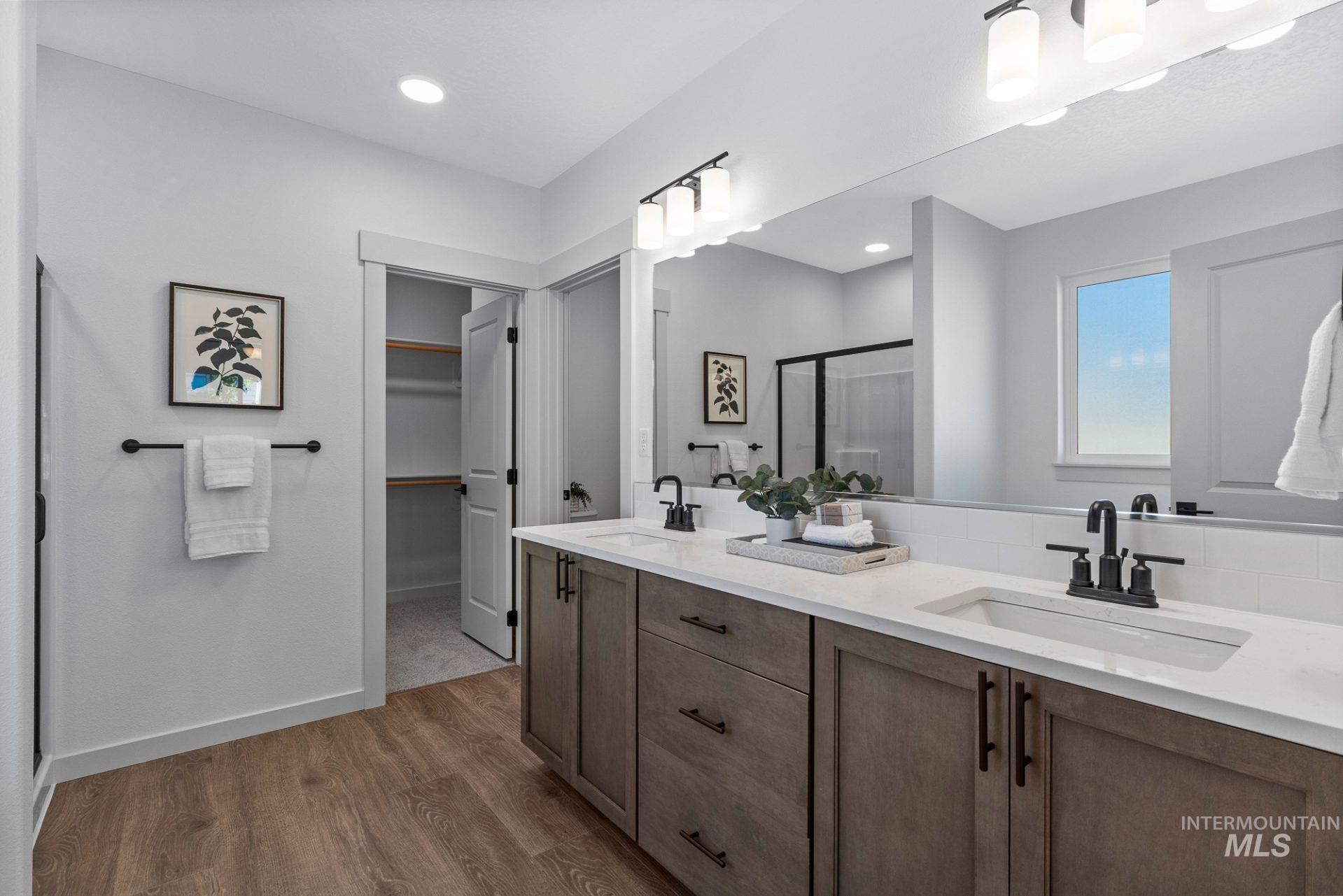 Bathroom with a spacious closet, double vanity, a stall shower, light wood-style floors, and recessed lighting