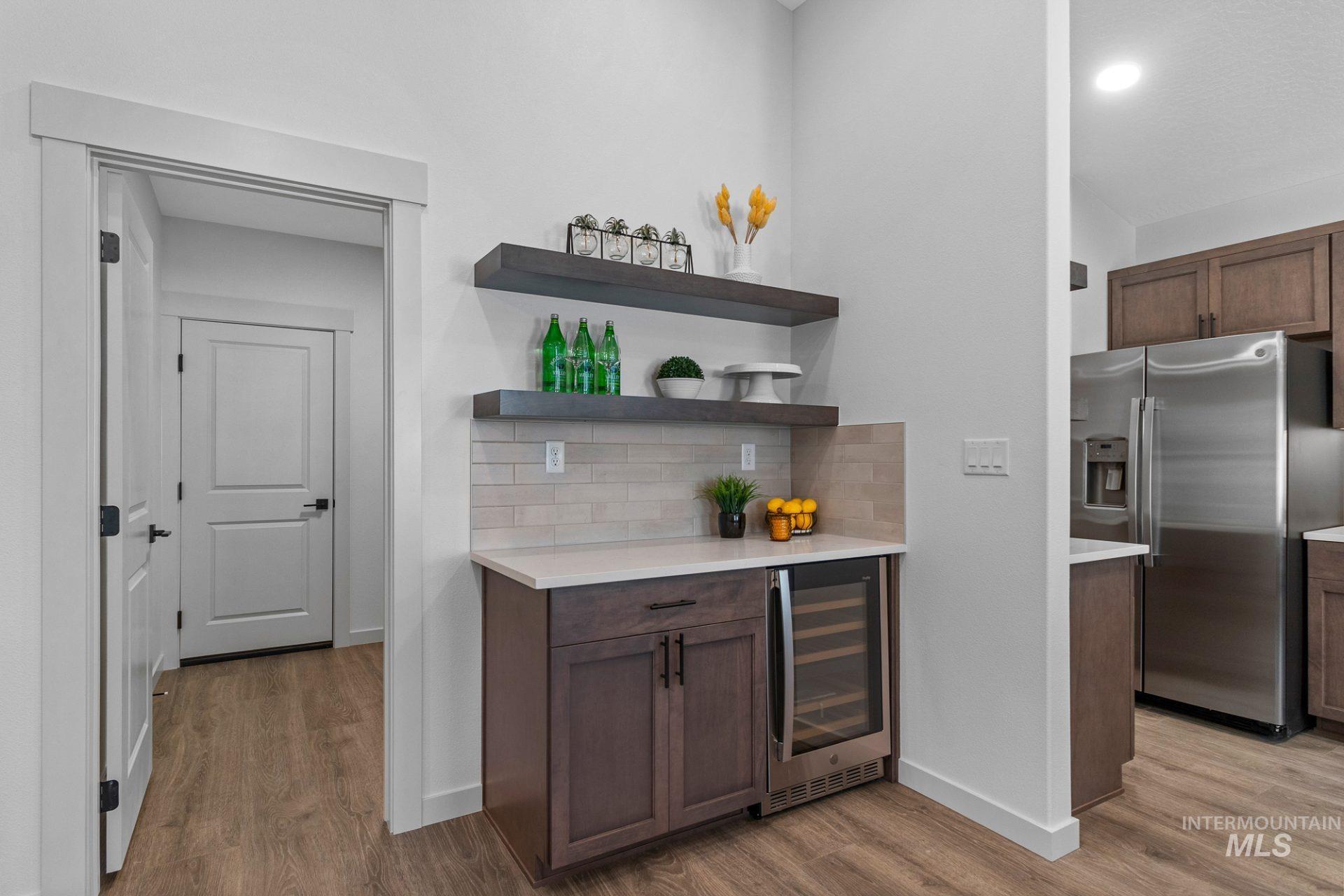 Indoor dry bar with stainless steel refrigerator with ice dispenser, open shelves, wine cooler, light wood-style flooring, and backsplash