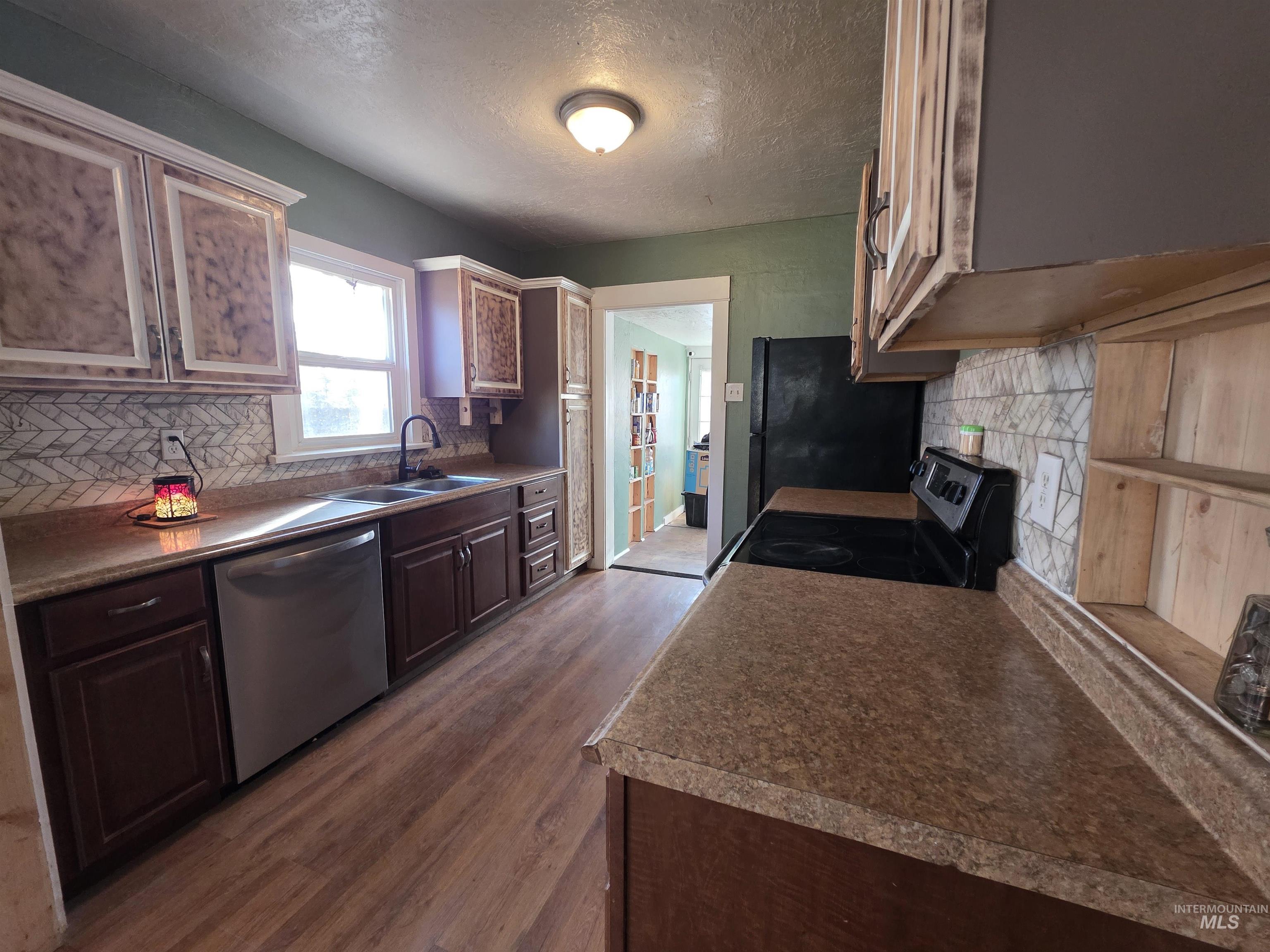 Kitchen featuring decorative backsplash, a textured ceiling, appliances with stainless steel finishes, dark wood-type flooring, and dark countertops