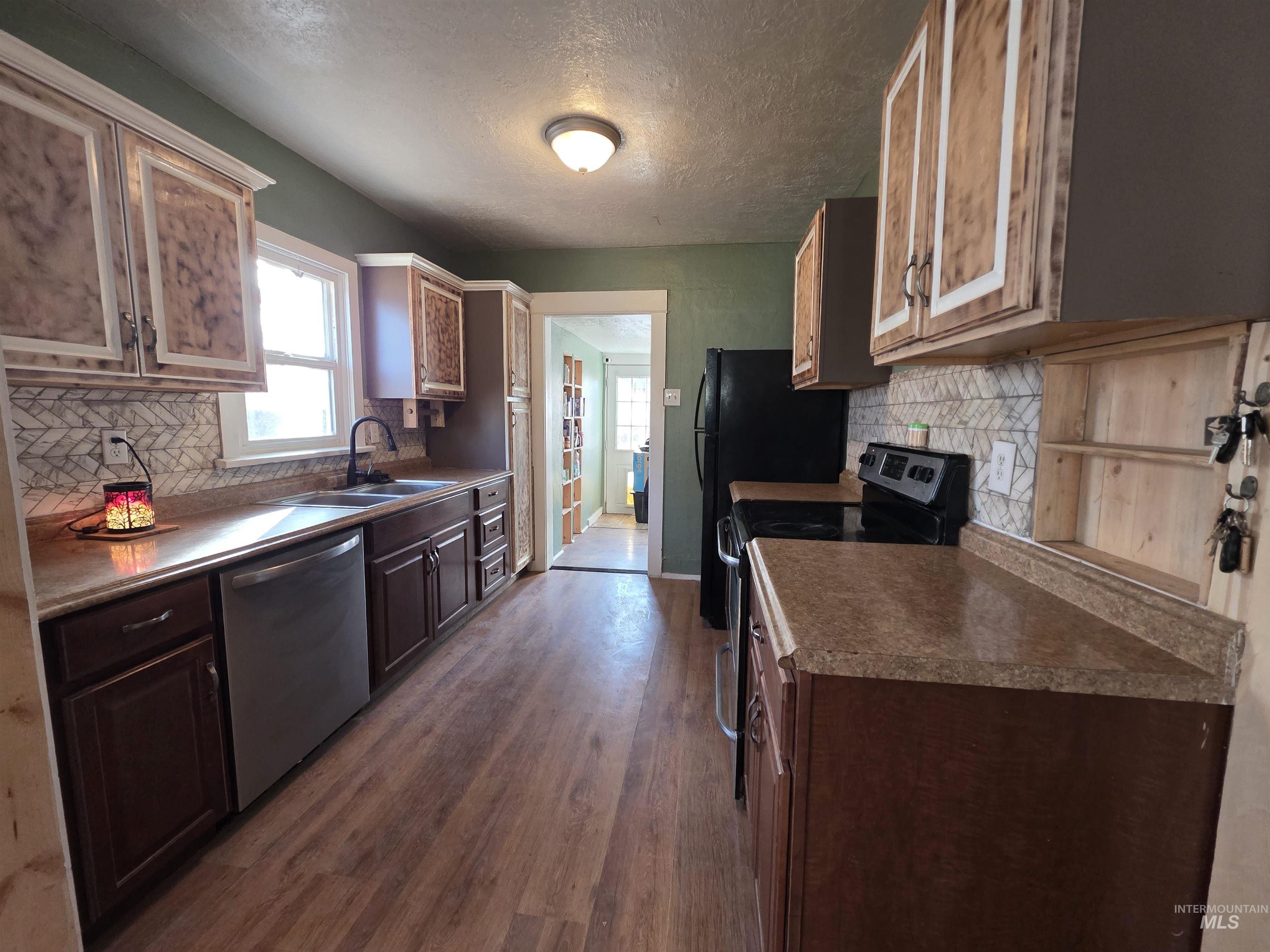 Kitchen featuring black electric range, backsplash, stainless steel dishwasher, a textured ceiling, and dark wood-type flooring