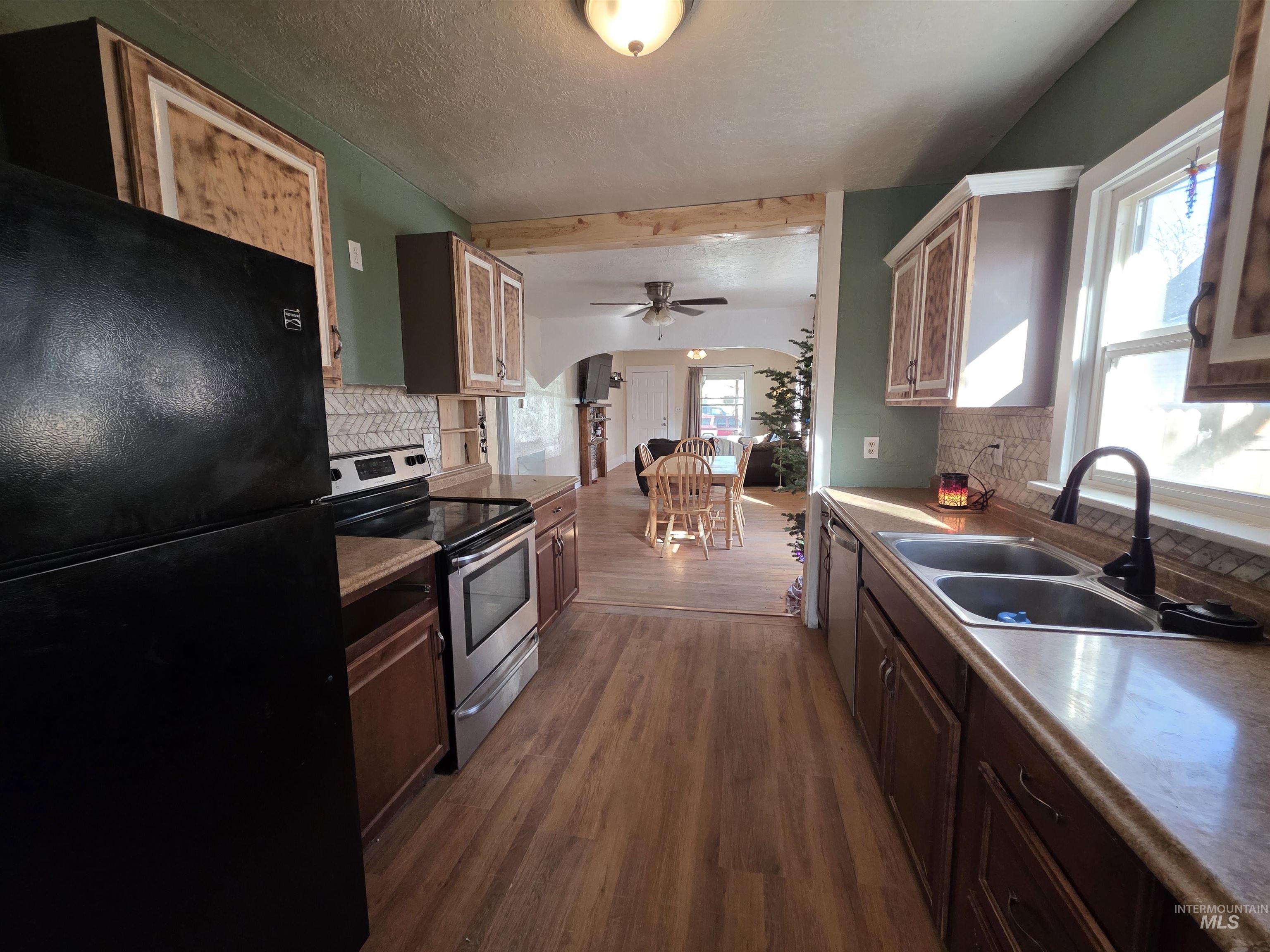 Kitchen with tasteful backsplash, appliances with stainless steel finishes, dark wood finished floors, ceiling fan, and a textured ceiling