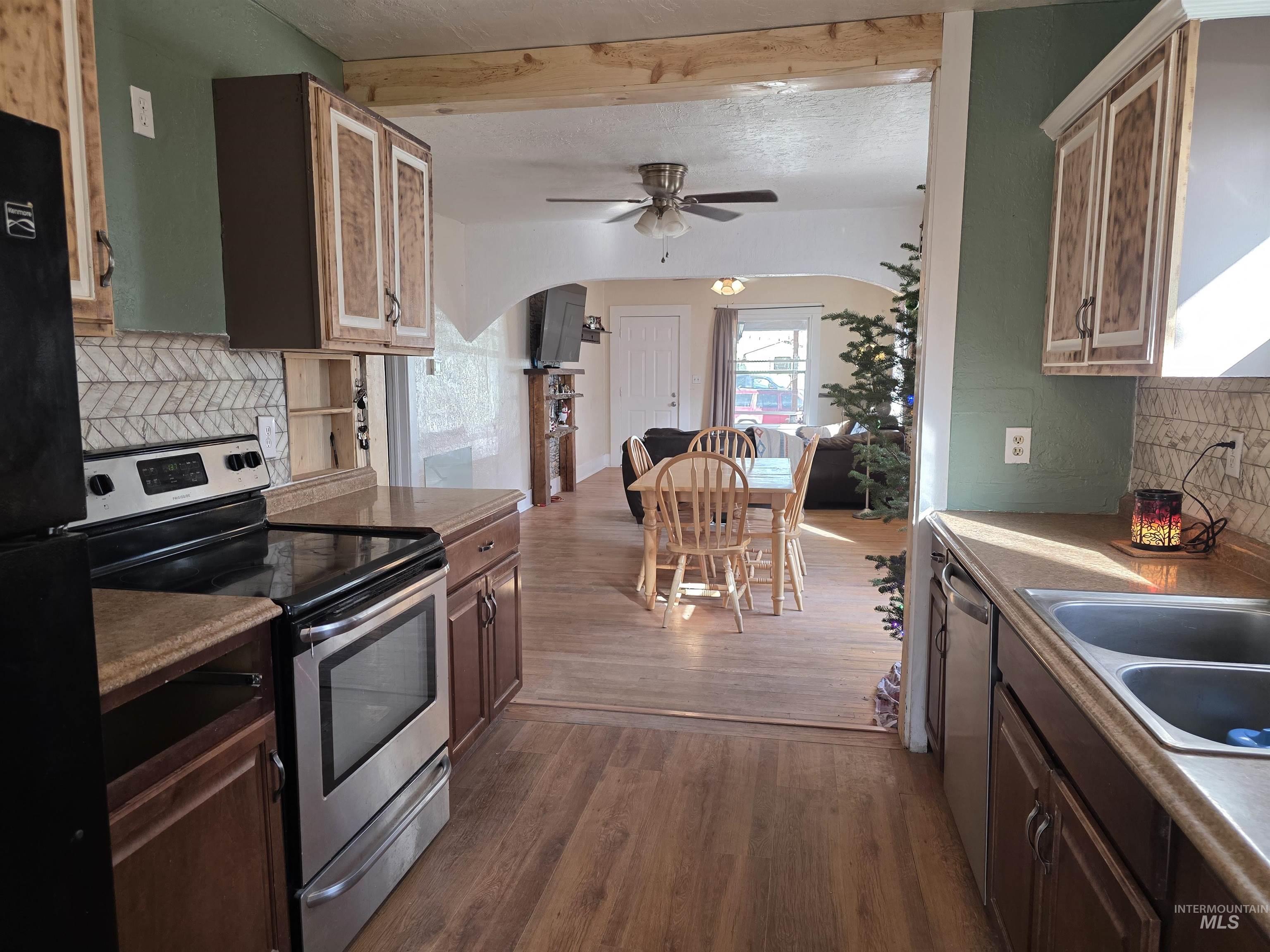 Kitchen featuring tasteful backsplash, appliances with stainless steel finishes, dark wood-style flooring, arched walkways, and beamed ceiling