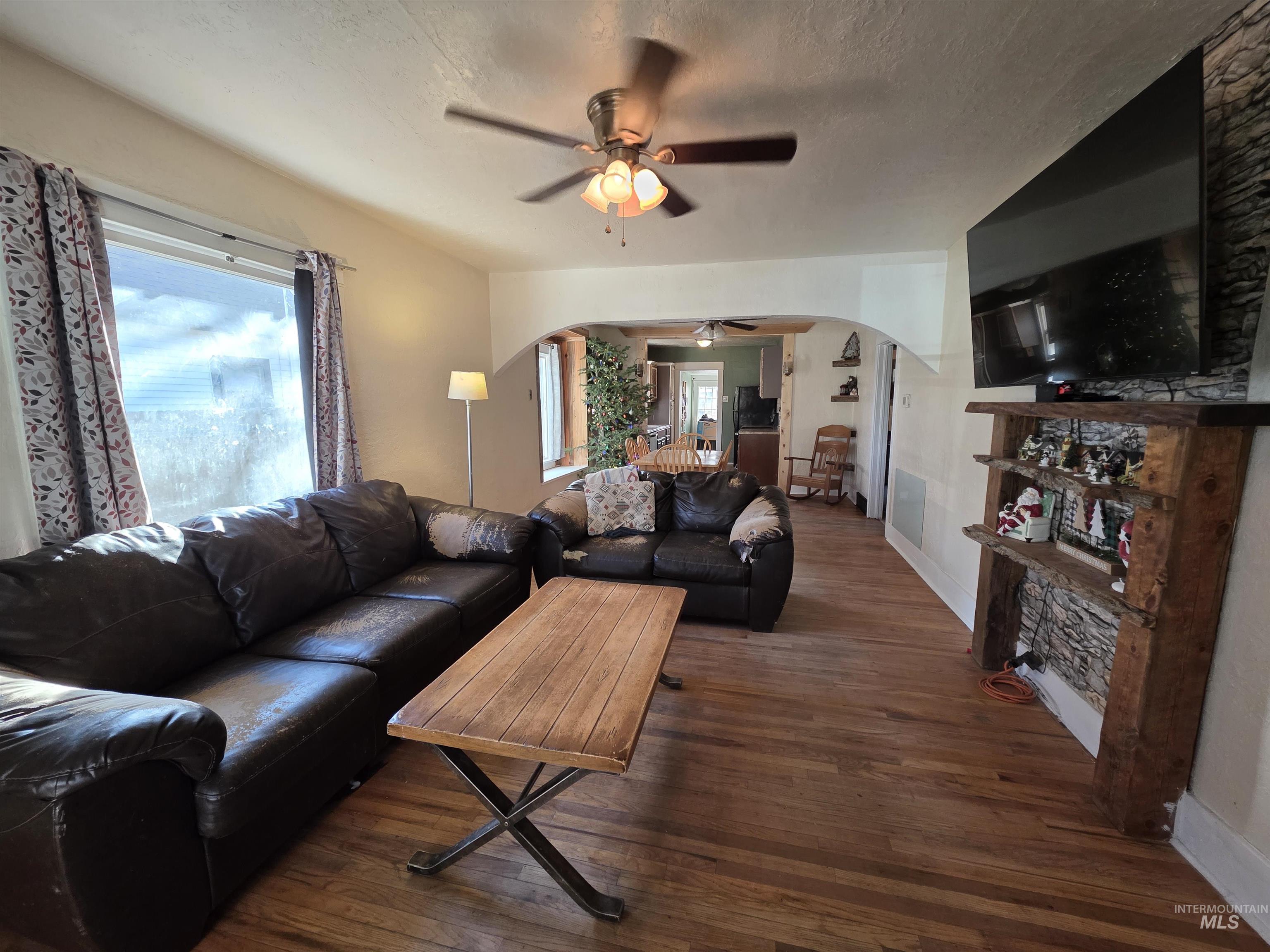 Living room featuring arched walkways, a ceiling fan, hardwood / wood-style floors, and a textured ceiling