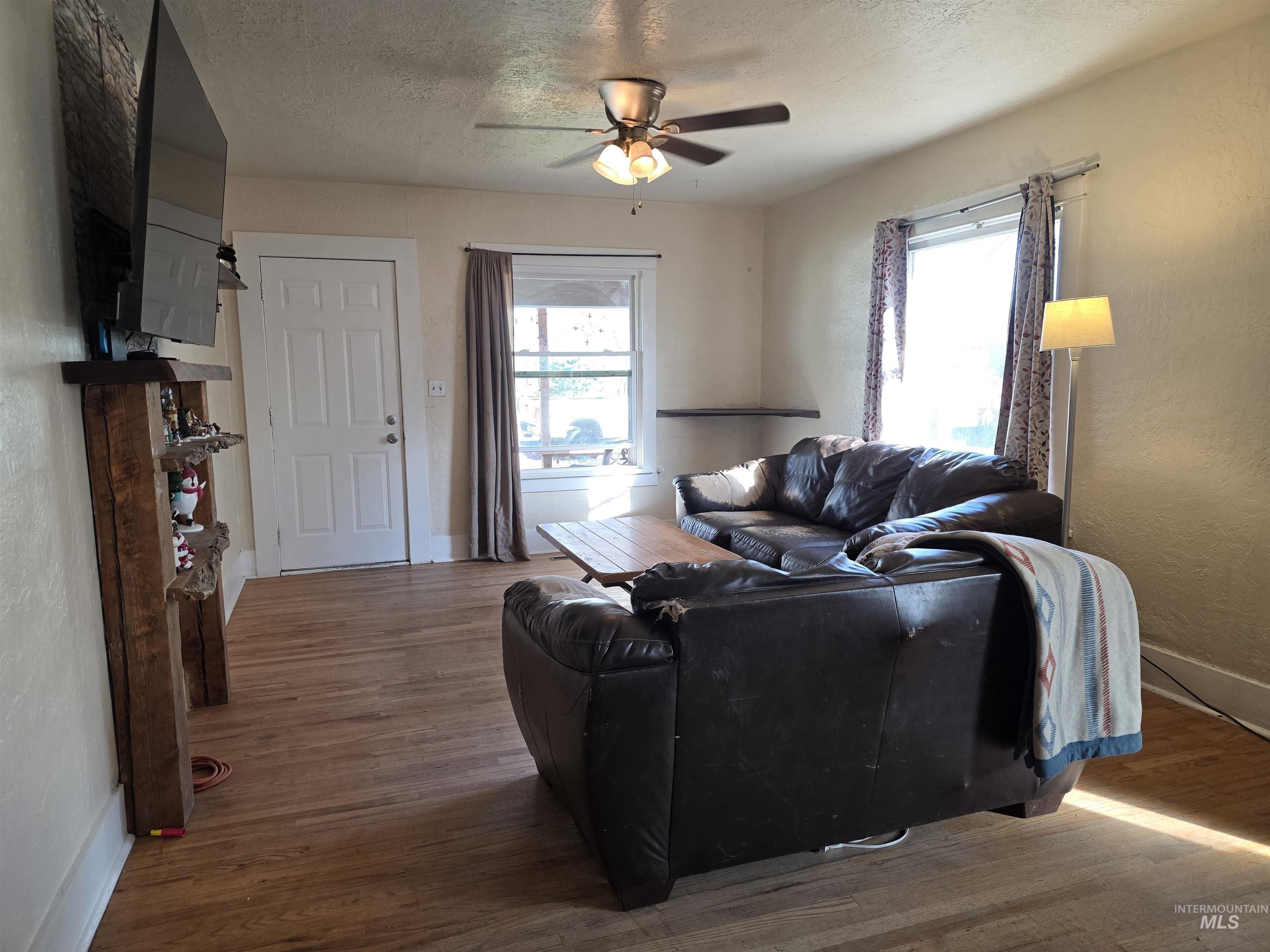 Living area with a textured ceiling, wood finished floors, and ceiling fan