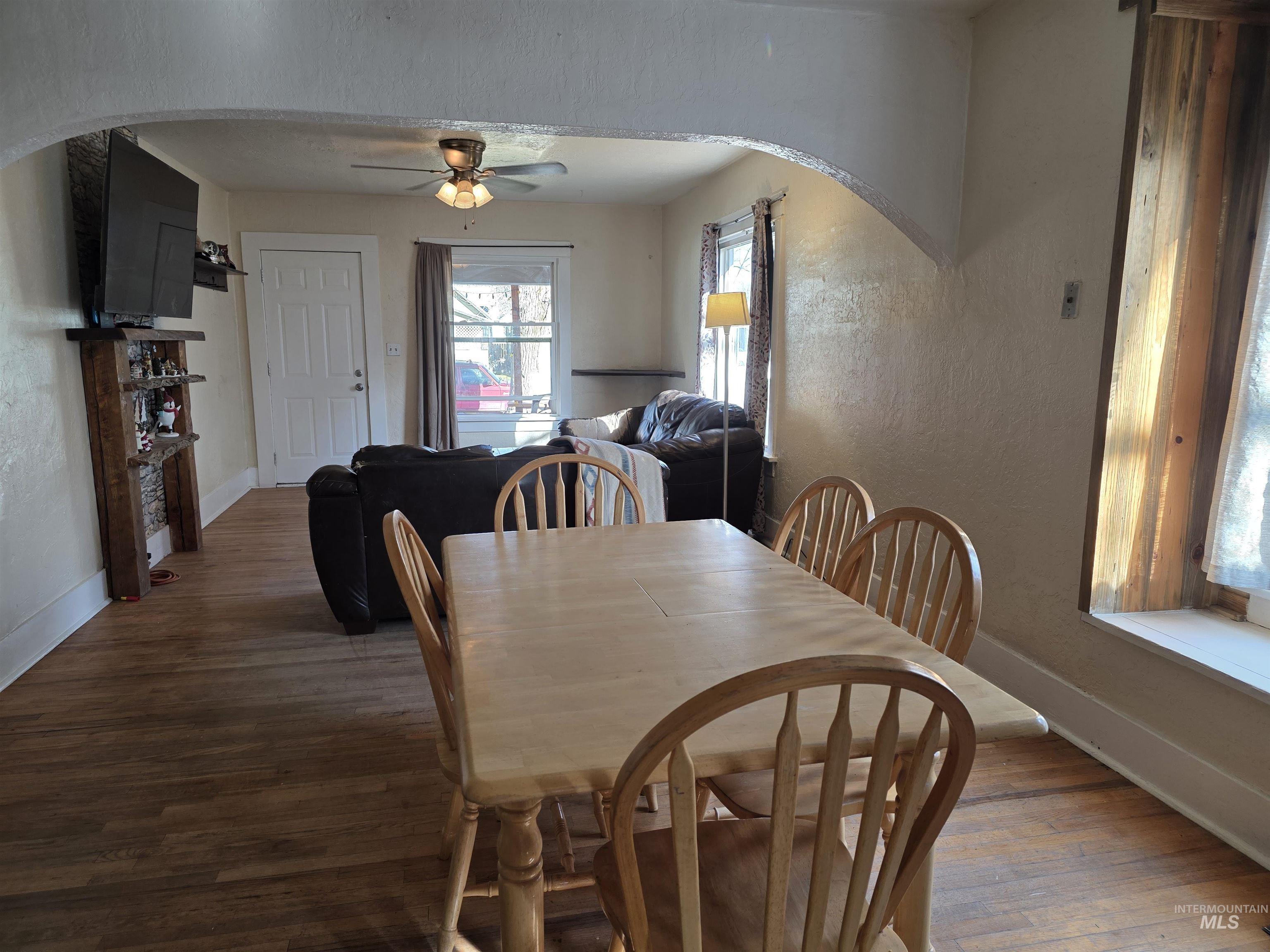 Dining space featuring arched walkways, hardwood / wood-style floors, ceiling fan, and a textured wall