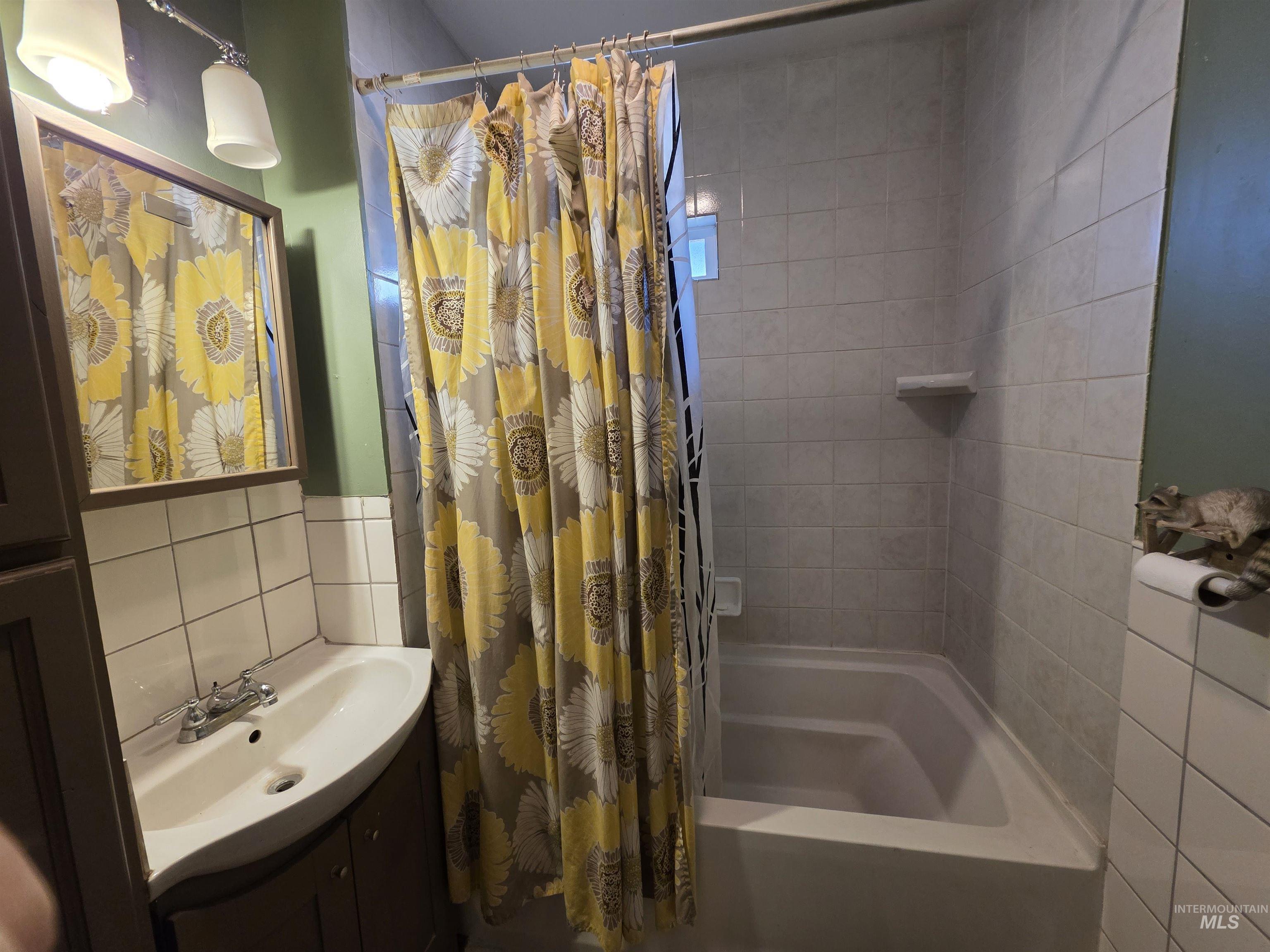 Bathroom with tile walls, vanity, shower / bathtub combination with curtain, and wainscoting