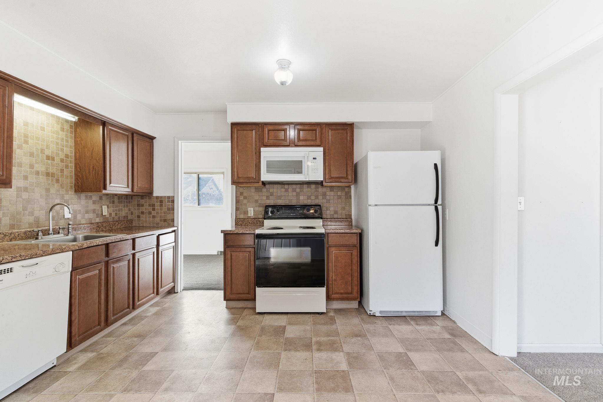 Kitchen featuring white appliances, decorative backsplash, brown cabinets, and light stone countertops