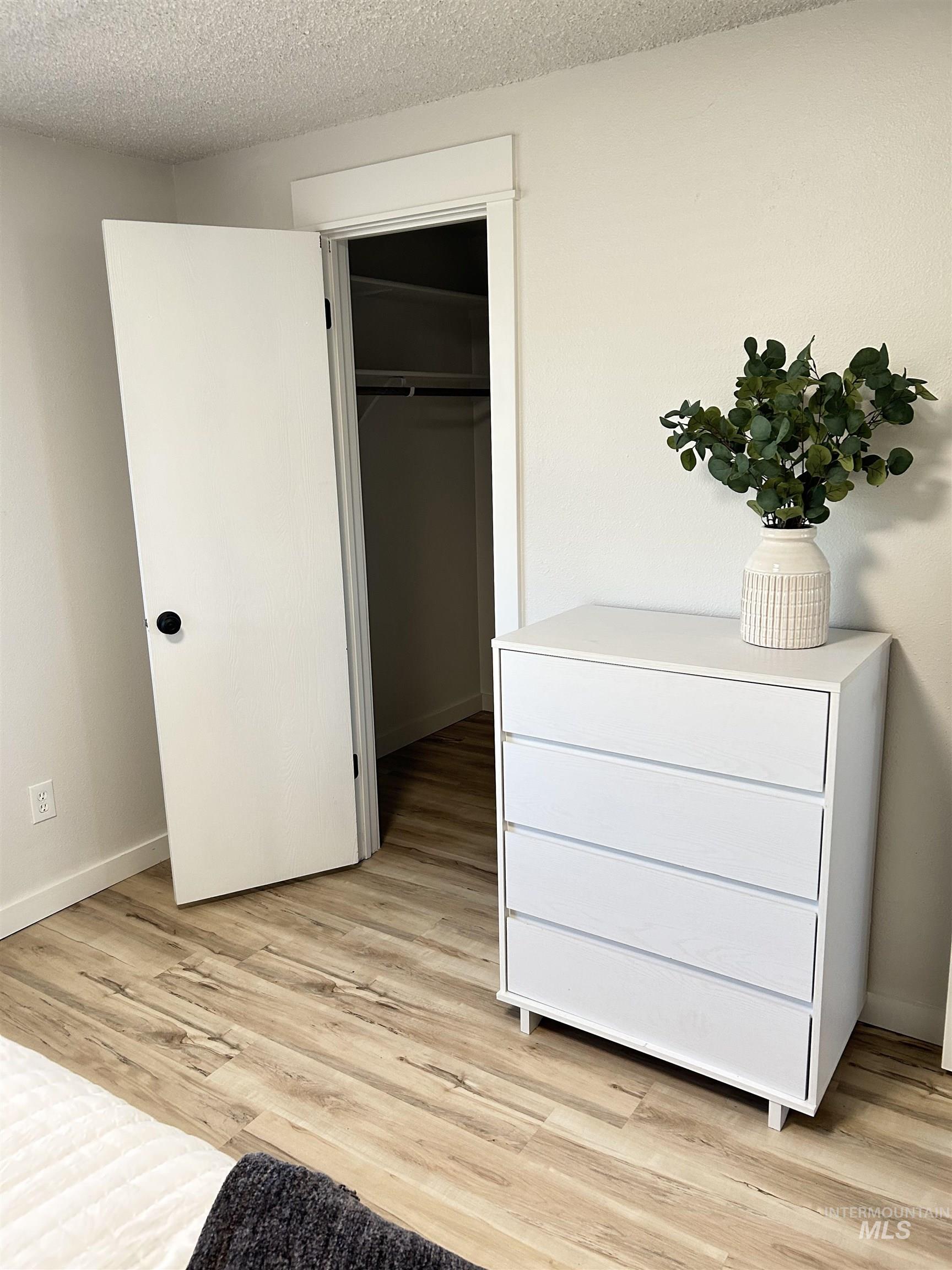 Bedroom with a spacious closet, a textured ceiling, and light wood-style floors
