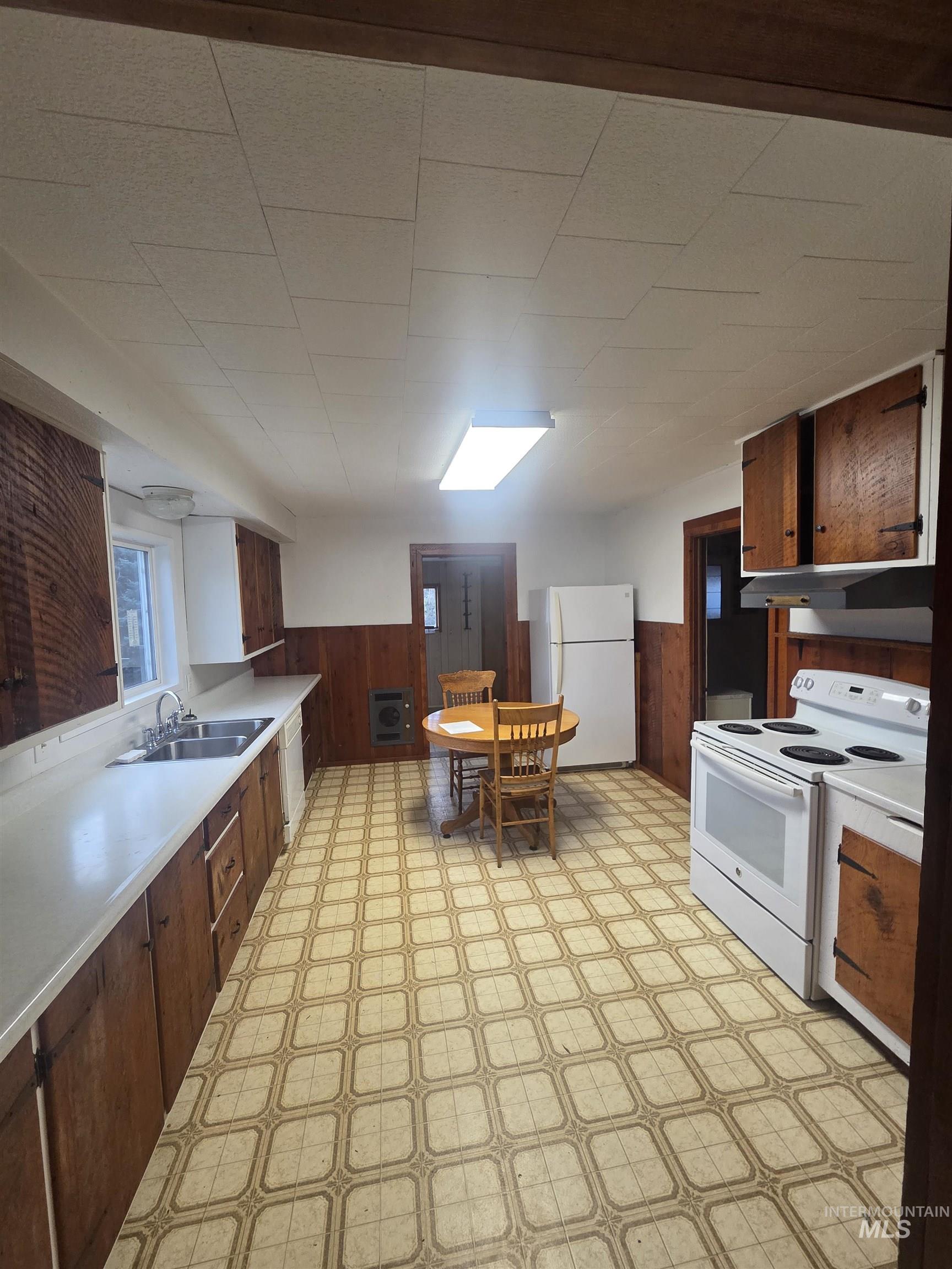 Kitchen with light floors, a wainscoted wall, wooden walls, white appliances, and light countertops