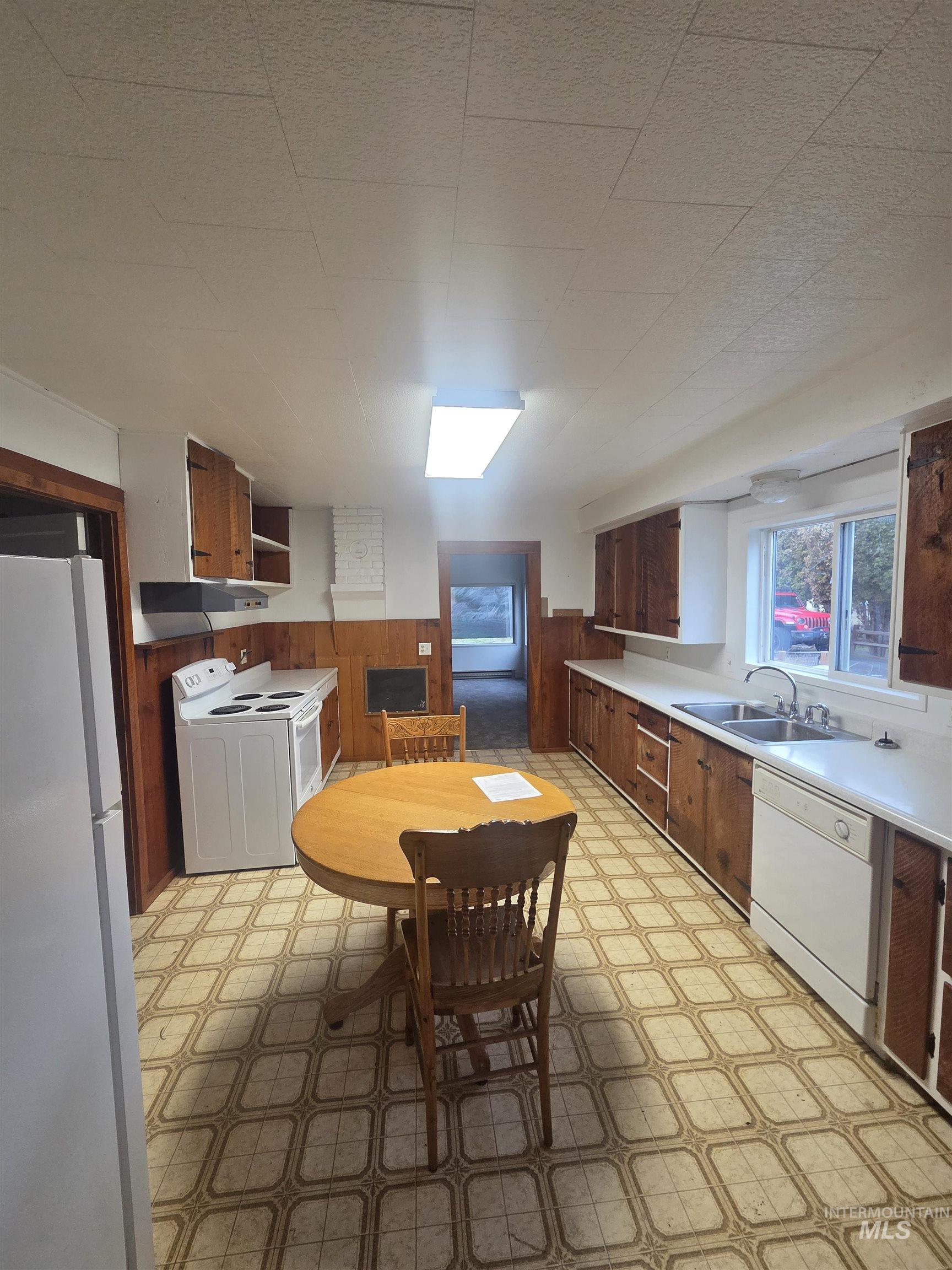 Kitchen featuring light floors, white appliances, wainscoting, light countertops, and wooden walls