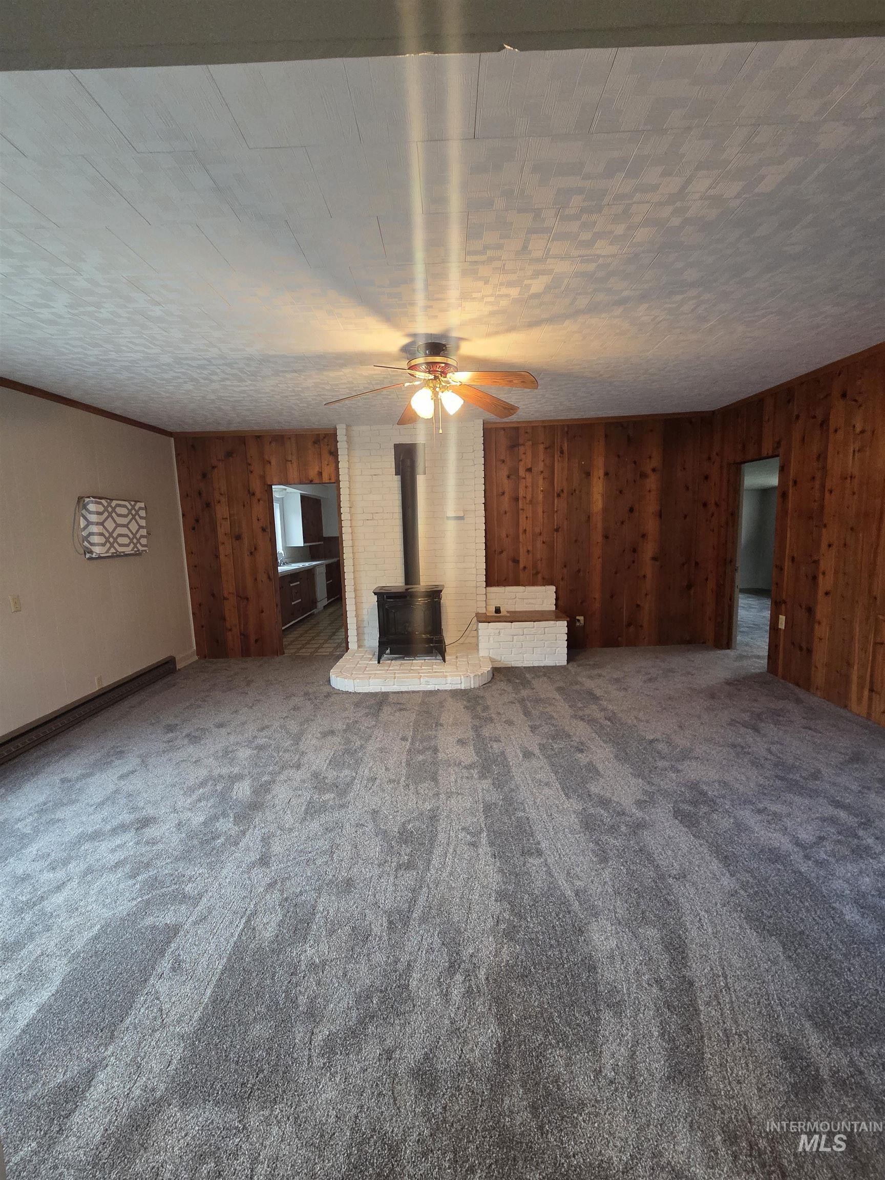 Unfurnished living room with wooden walls, a wood stove, ceiling fan, and carpet floors