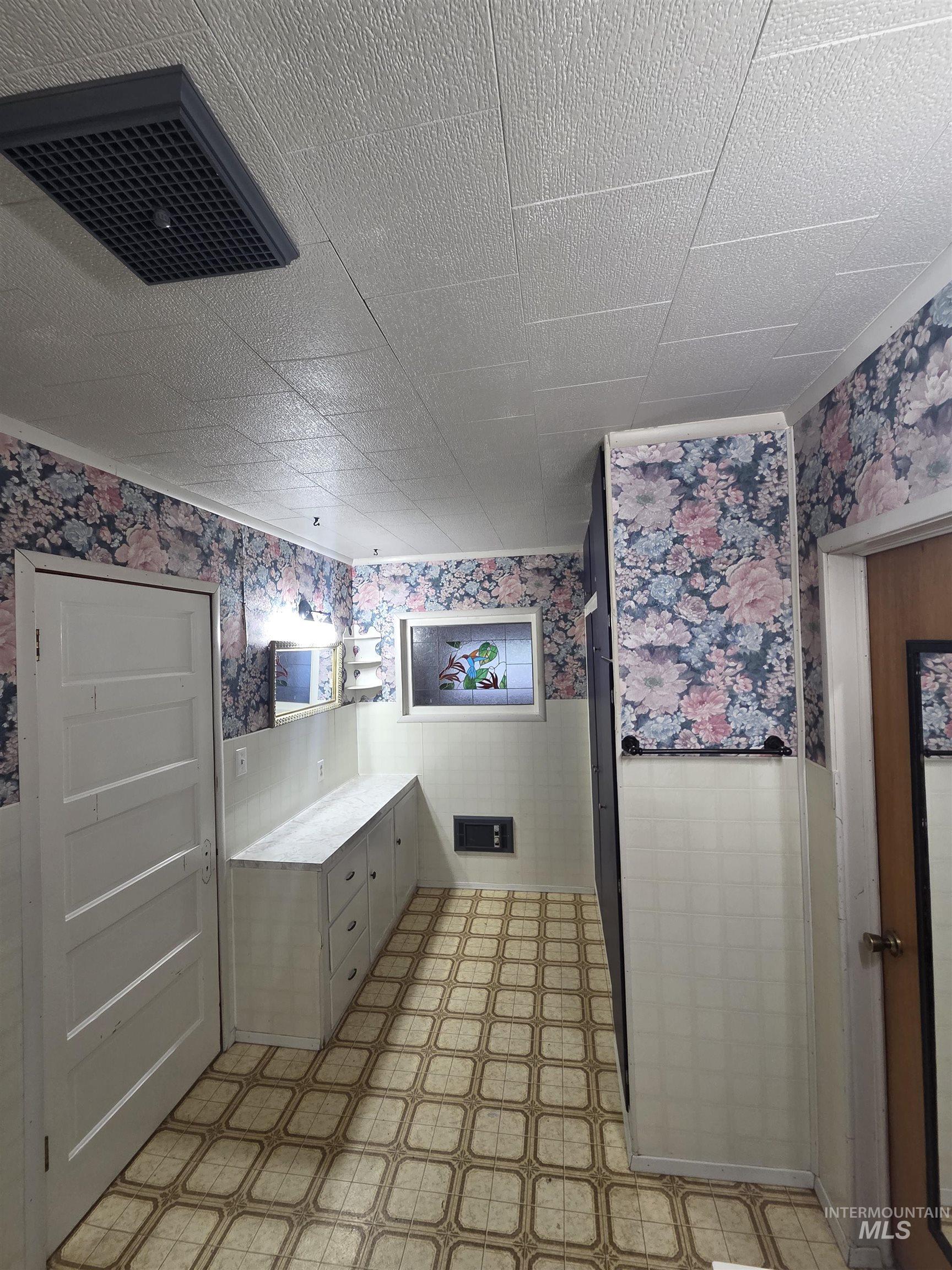 Bathroom featuring wallpapered walls, wainscoting, light flooring, and vanity