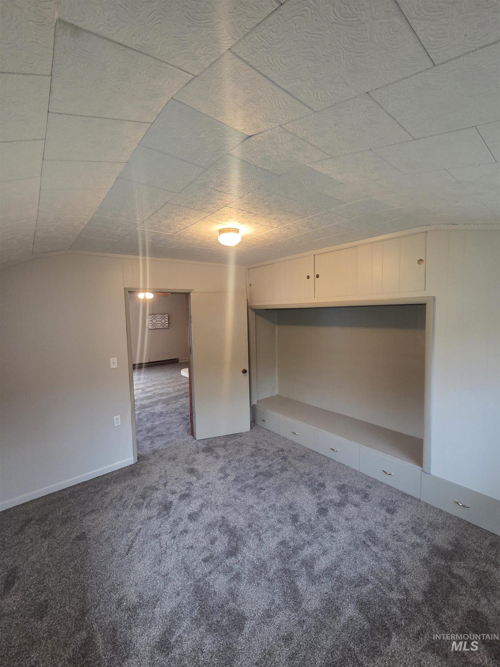 Spare room featuring dark colored carpet and vaulted ceiling
