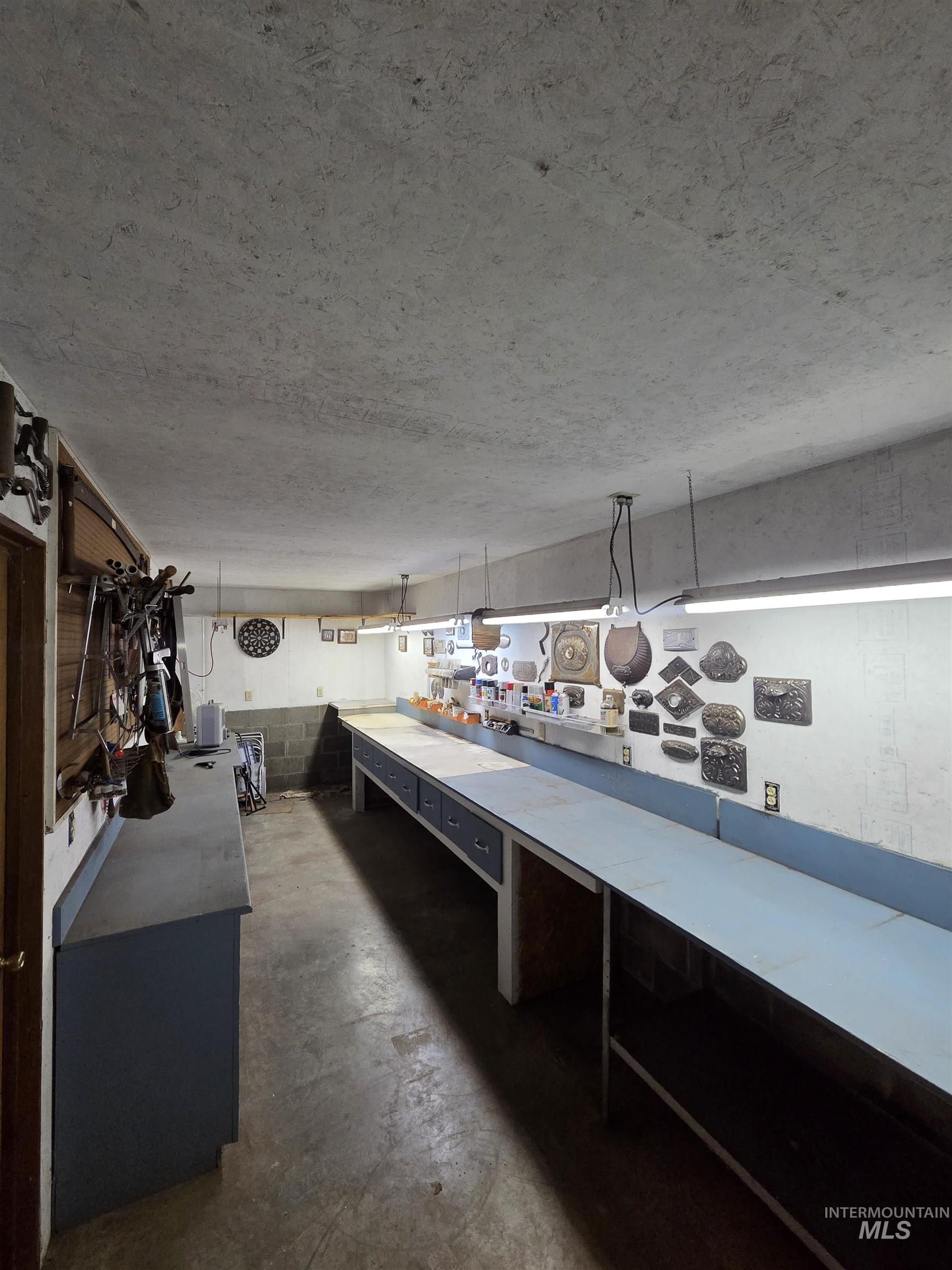 Bar area with concrete block wall, unfinished concrete flooring, light countertops, a workshop area, and pendant lighting