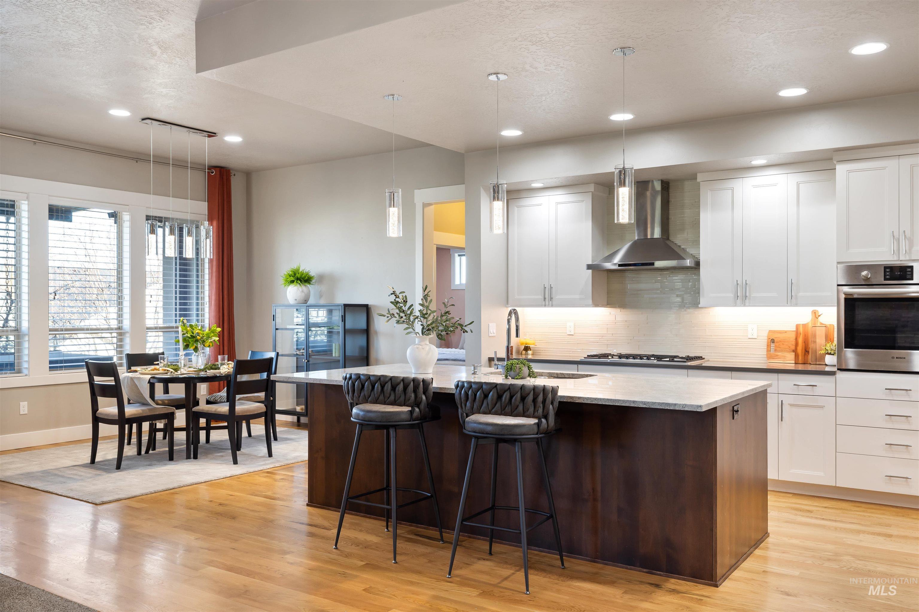 Kitchen with pendant lighting, oven, wall chimney exhaust hood, backsplash, and a breakfast bar area