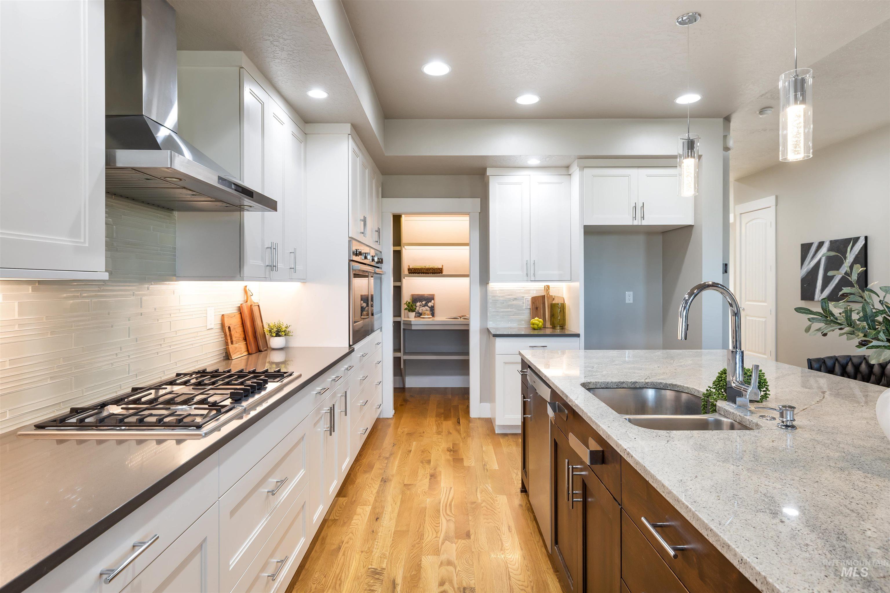 Kitchen with wall chimney exhaust hood, light wood-type flooring, white cabinetry, decorative light fixtures, and dark stone countertops