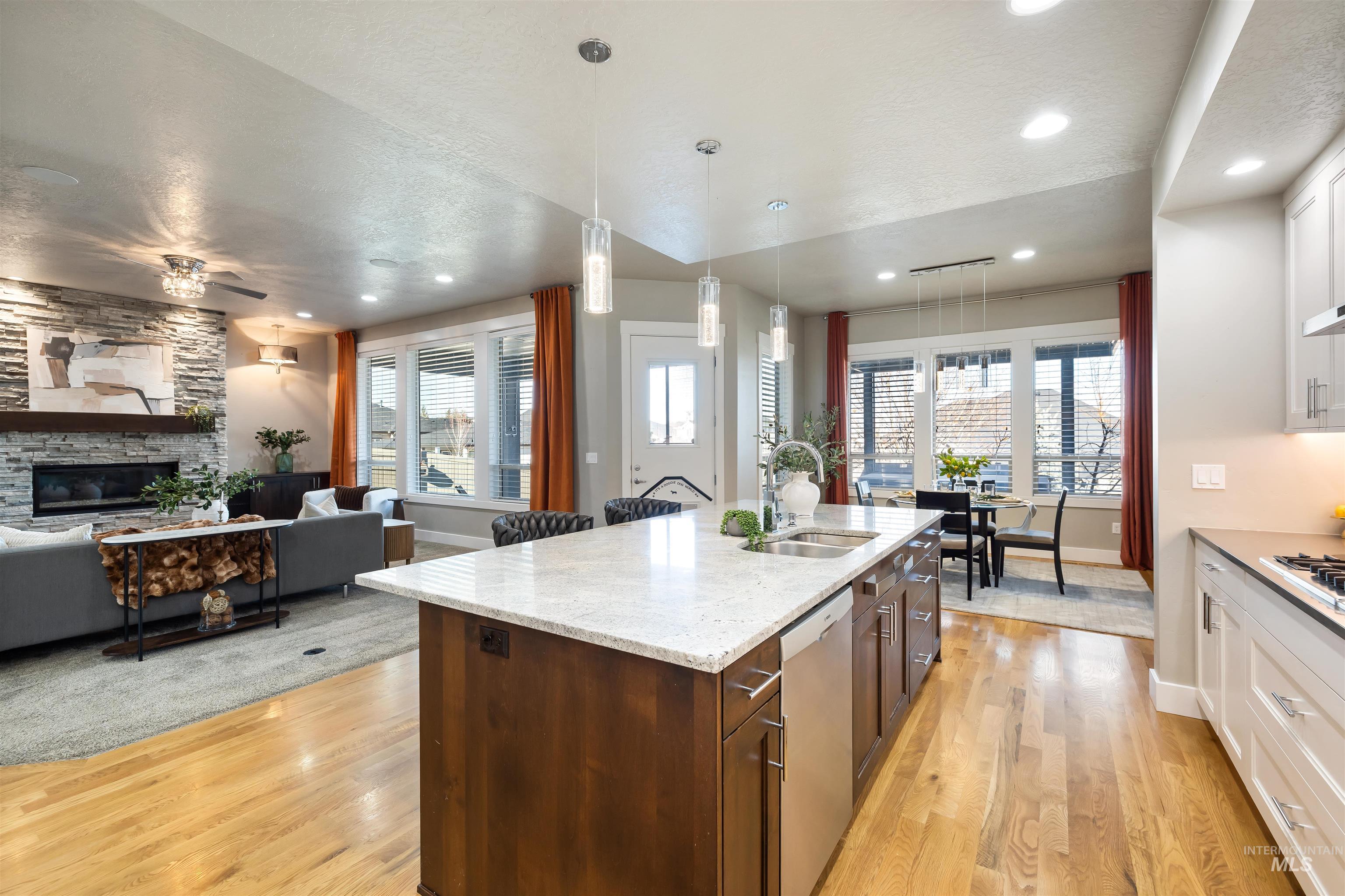 Kitchen featuring decorative light fixtures, white cabinetry, a fireplace, a kitchen island with sink, and light wood-style floors