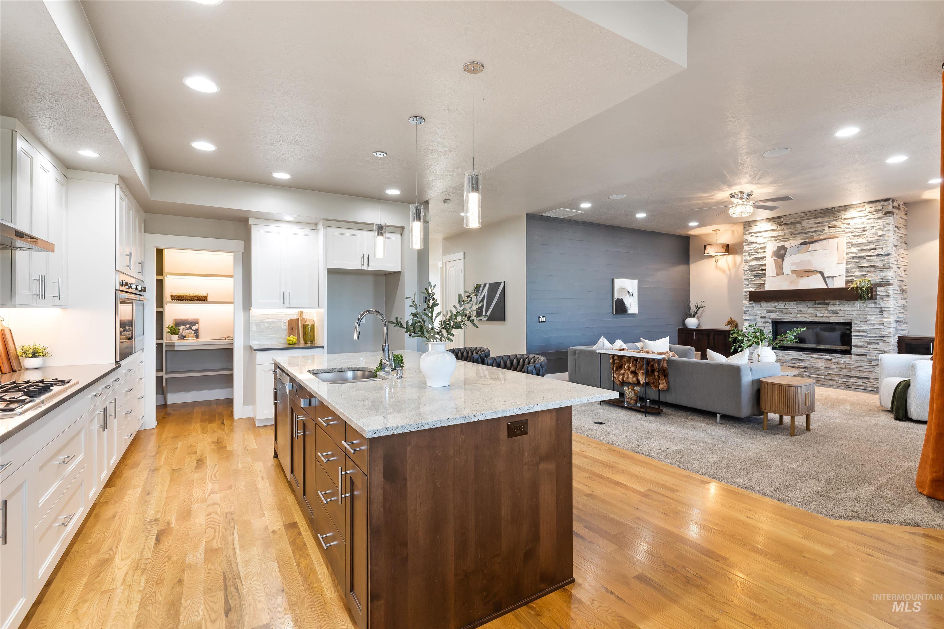 Kitchen featuring recessed lighting, pendant lighting, light stone counters, an island with sink, and white cabinetry