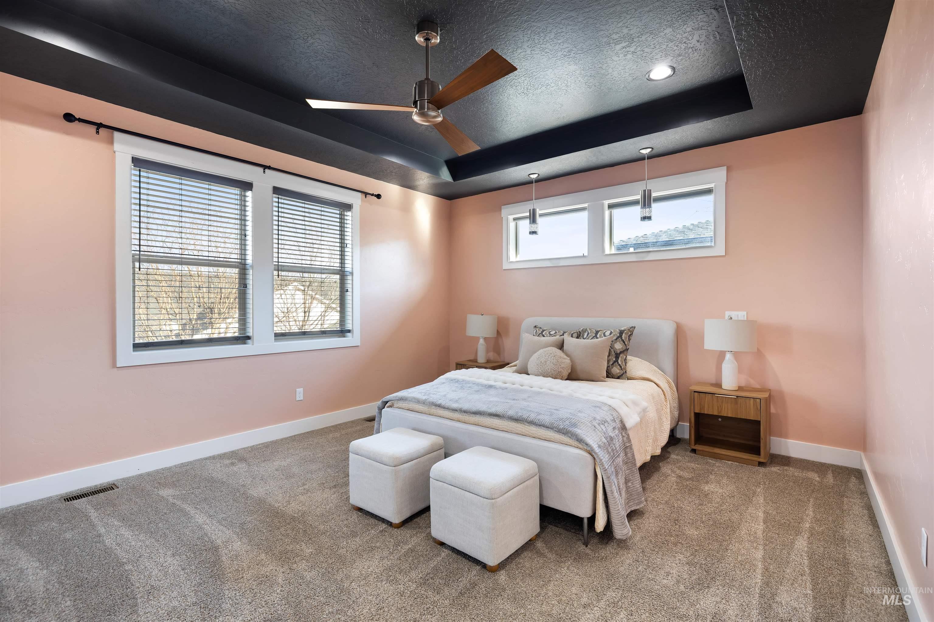 Carpeted bedroom featuring a textured ceiling, a tray ceiling, and a ceiling fan