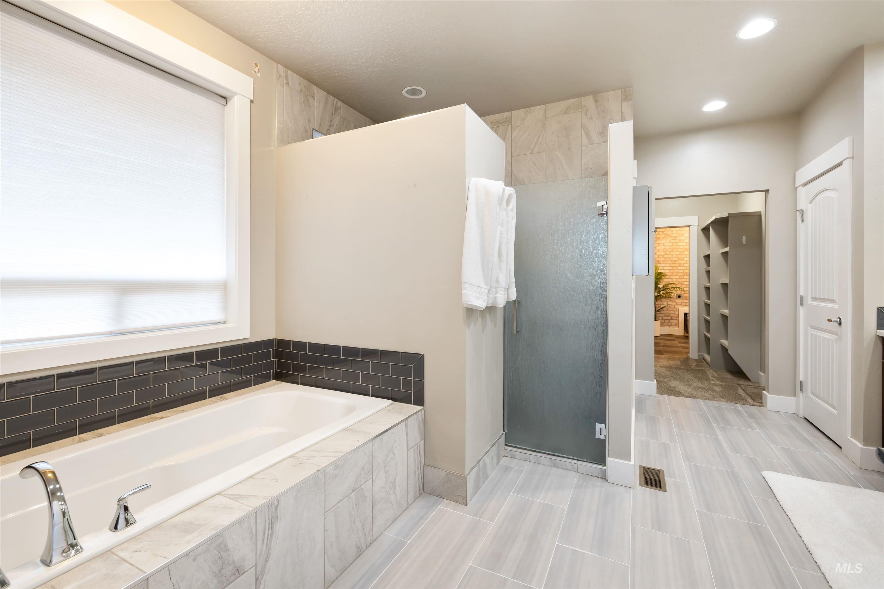 Bathroom featuring a walk in closet, a stall shower, a garden tub, and recessed lighting
