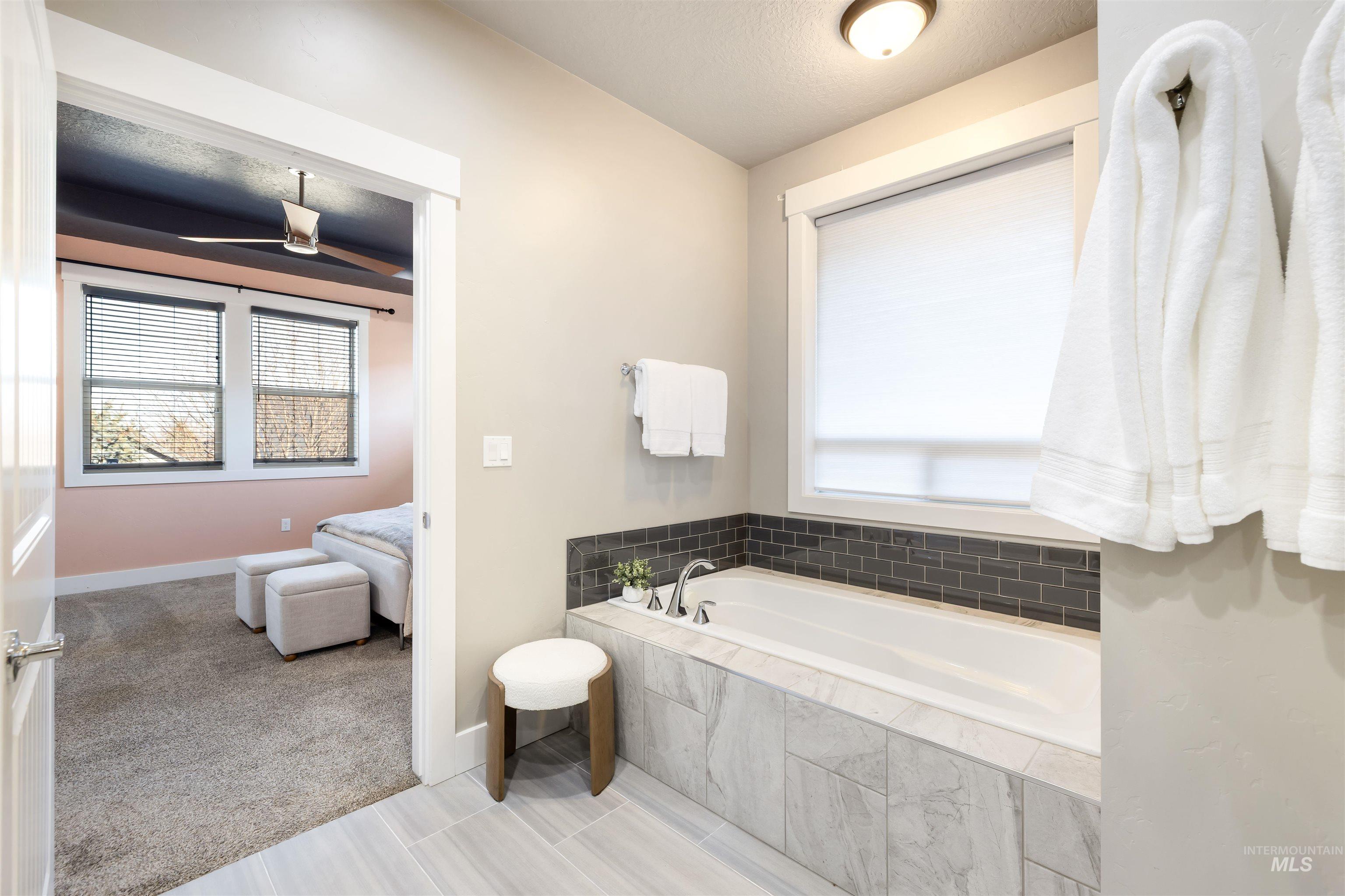 Ensuite bathroom featuring a garden tub, light carpet, ceiling fan, and a textured ceiling