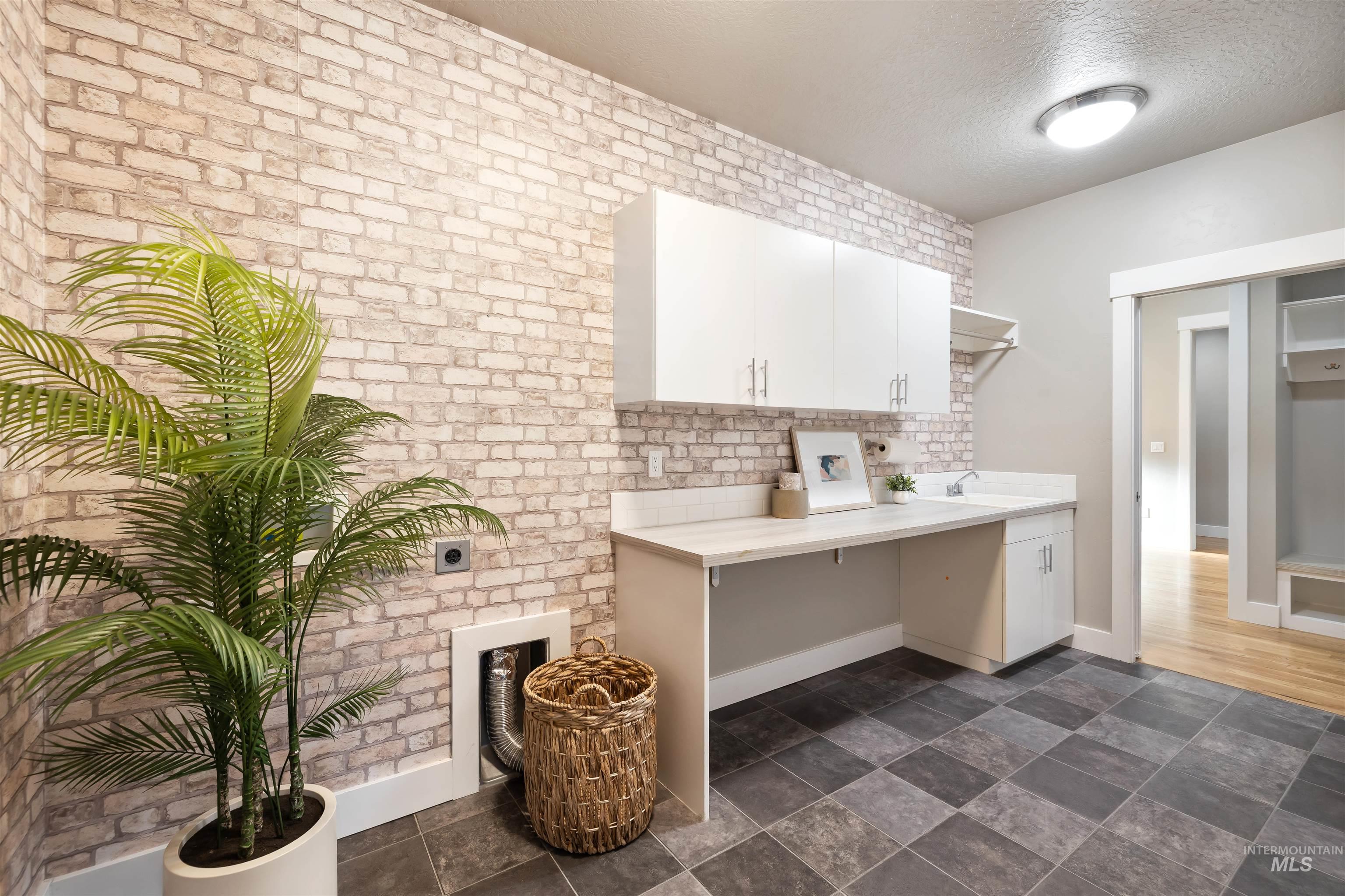 Laundry room featuring a textured ceiling, stone finish floors, brick wall, and electric dryer hookup