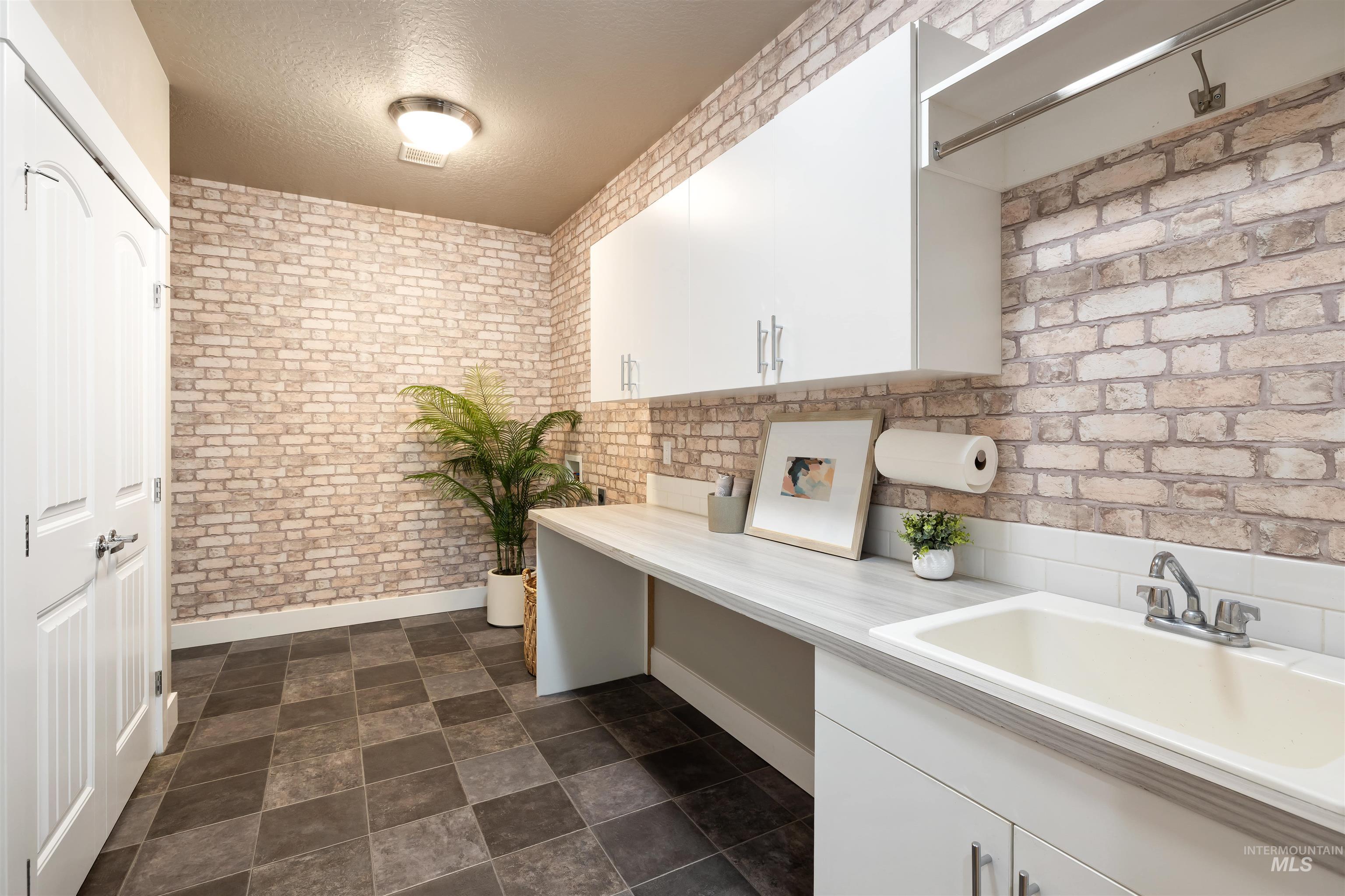 Laundry area featuring brick wall, a textured ceiling, and stone finish flooring
