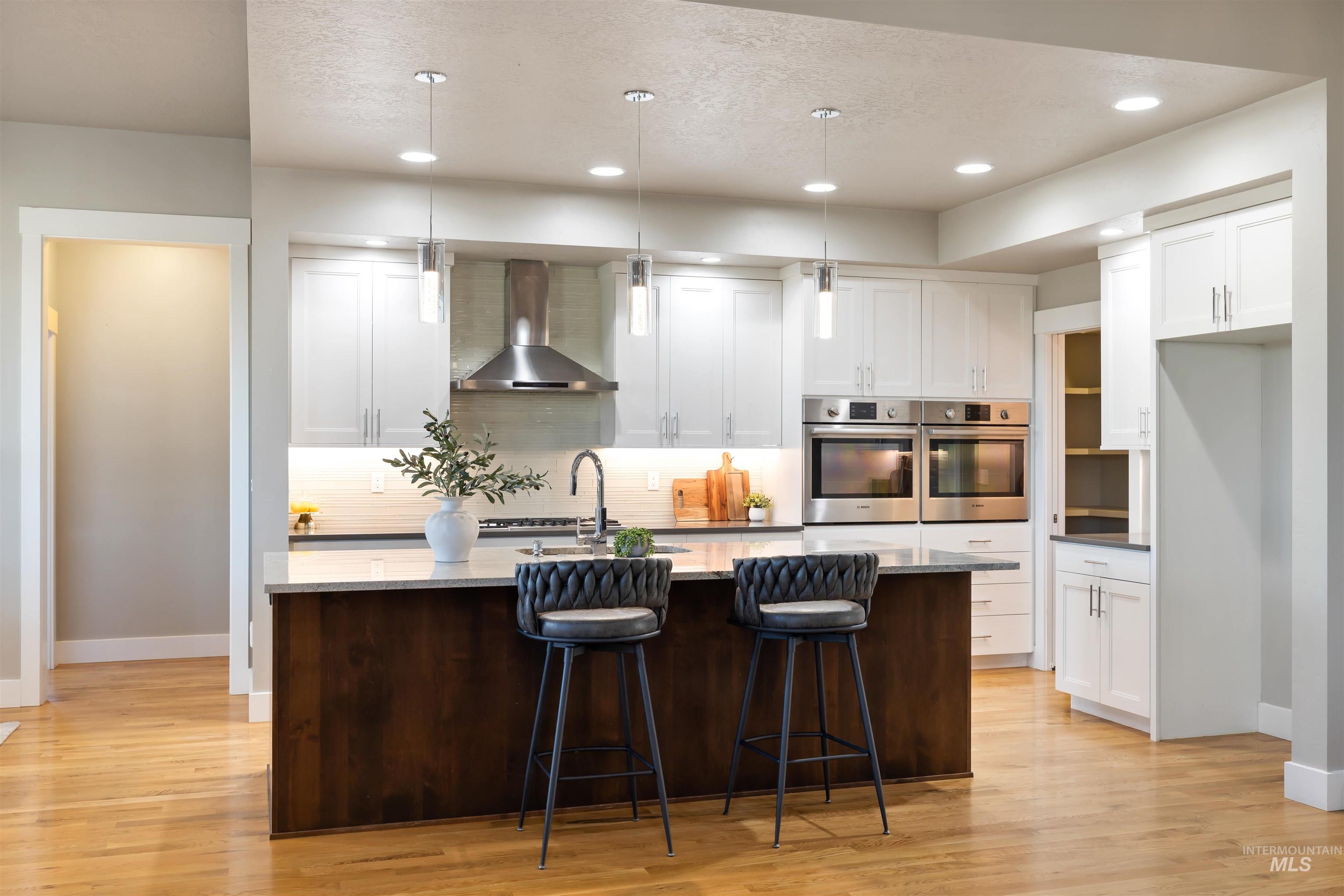 Kitchen featuring hanging light fixtures, white cabinets, wall chimney range hood, dark brown cabinets, and recessed lighting