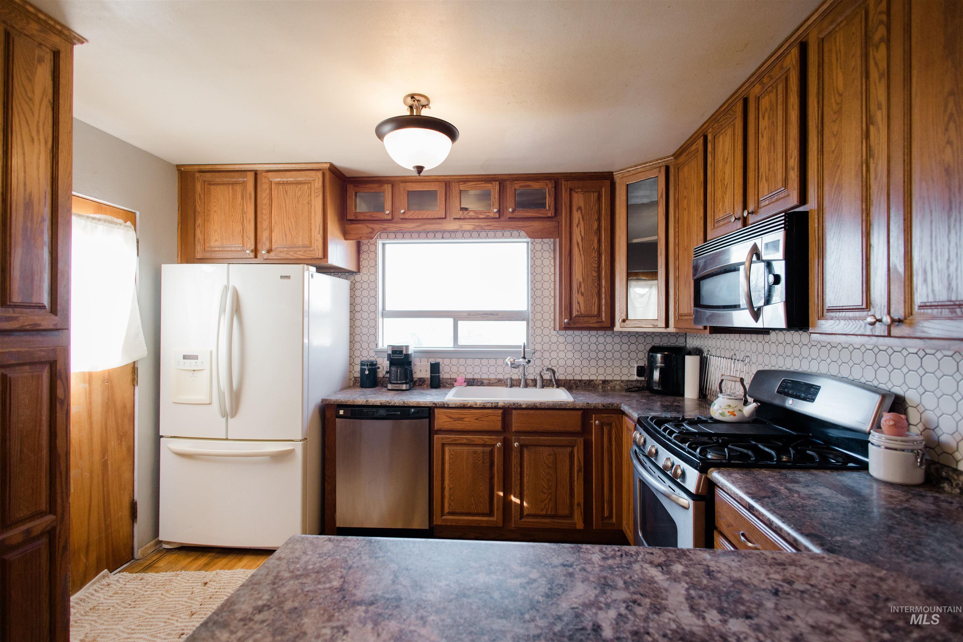 Kitchen with stainless steel appliances, brown cabinets, glass insert cabinets, and tasteful backsplash