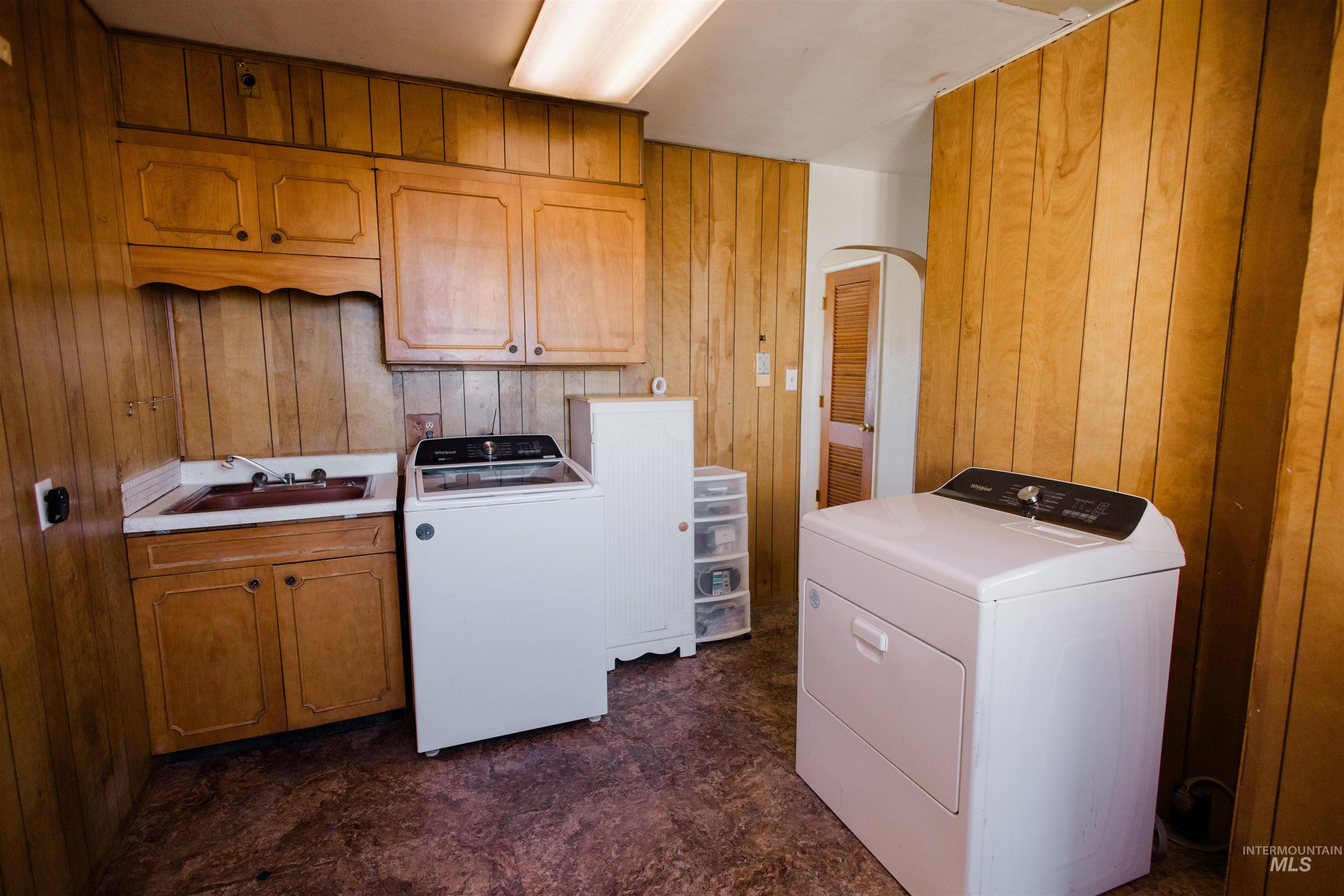 Laundry area featuring wood walls, cabinet space, dark flooring, and arched walkways