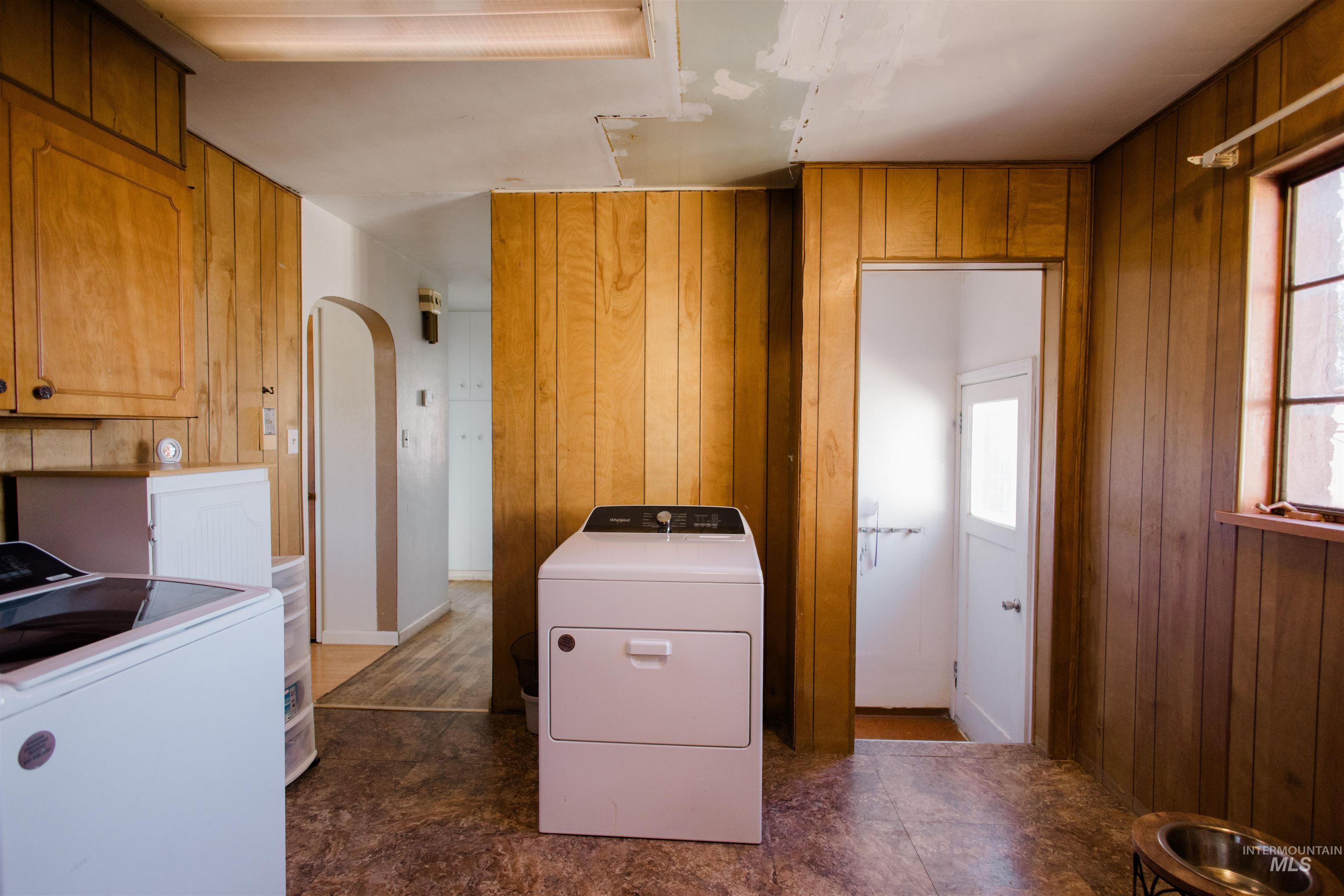 Laundry area featuring plenty of natural light, wood walls, arched walkways, and separate washer and dryer
