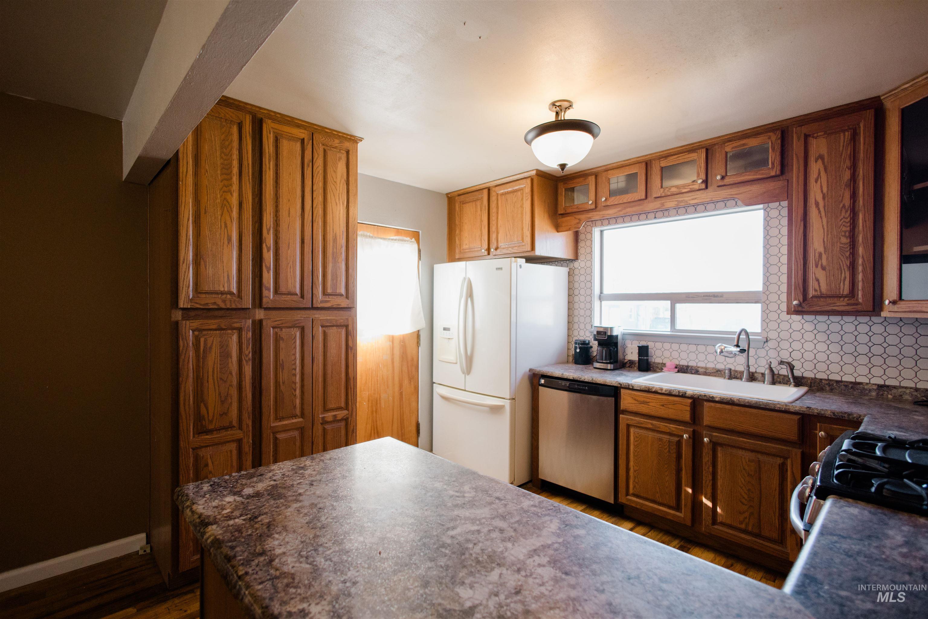 Kitchen featuring dark countertops, glass insert cabinets, dark wood finished floors, and dishwasher