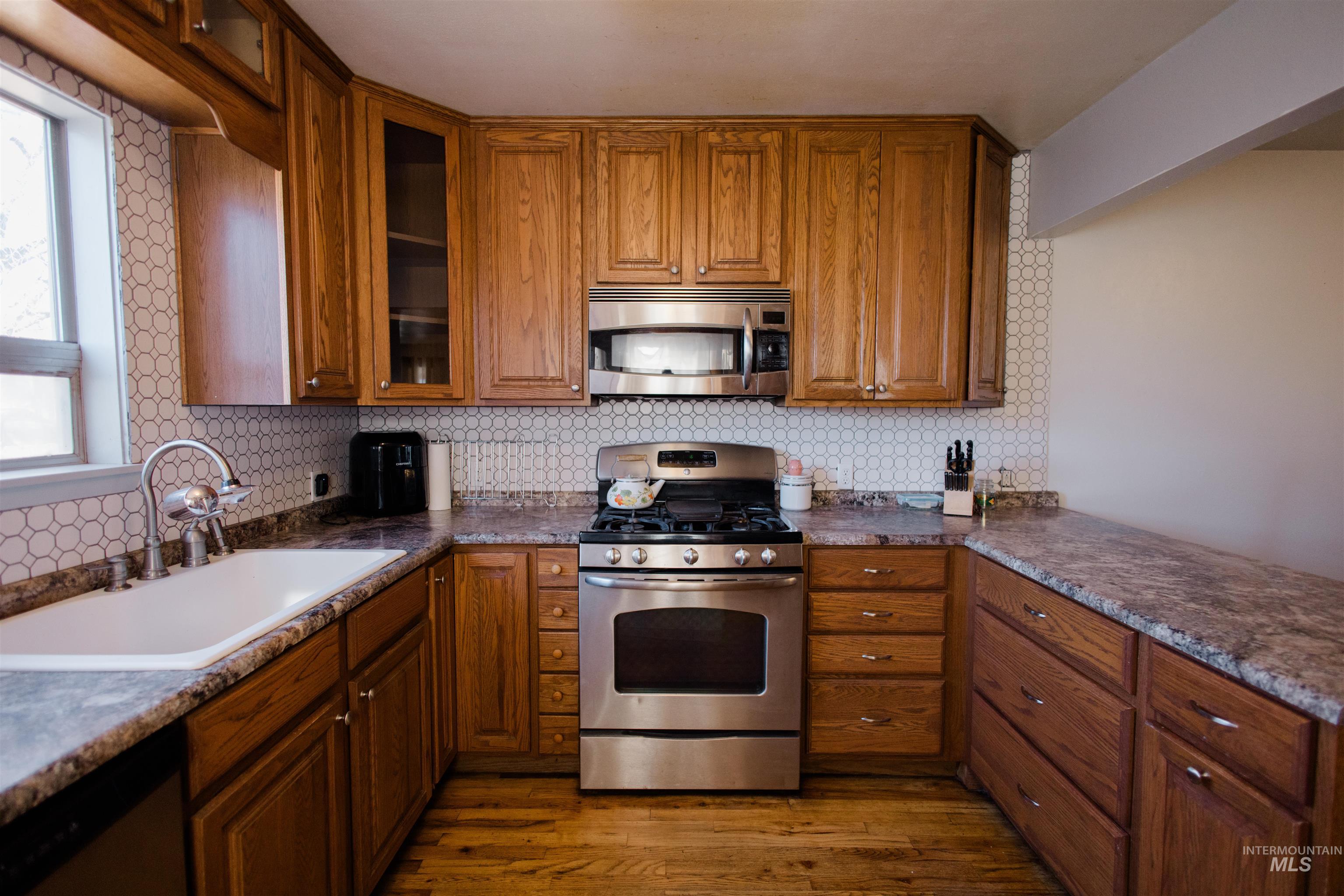 Kitchen featuring appliances with stainless steel finishes, brown cabinets, dark wood-style flooring, and decorative backsplash