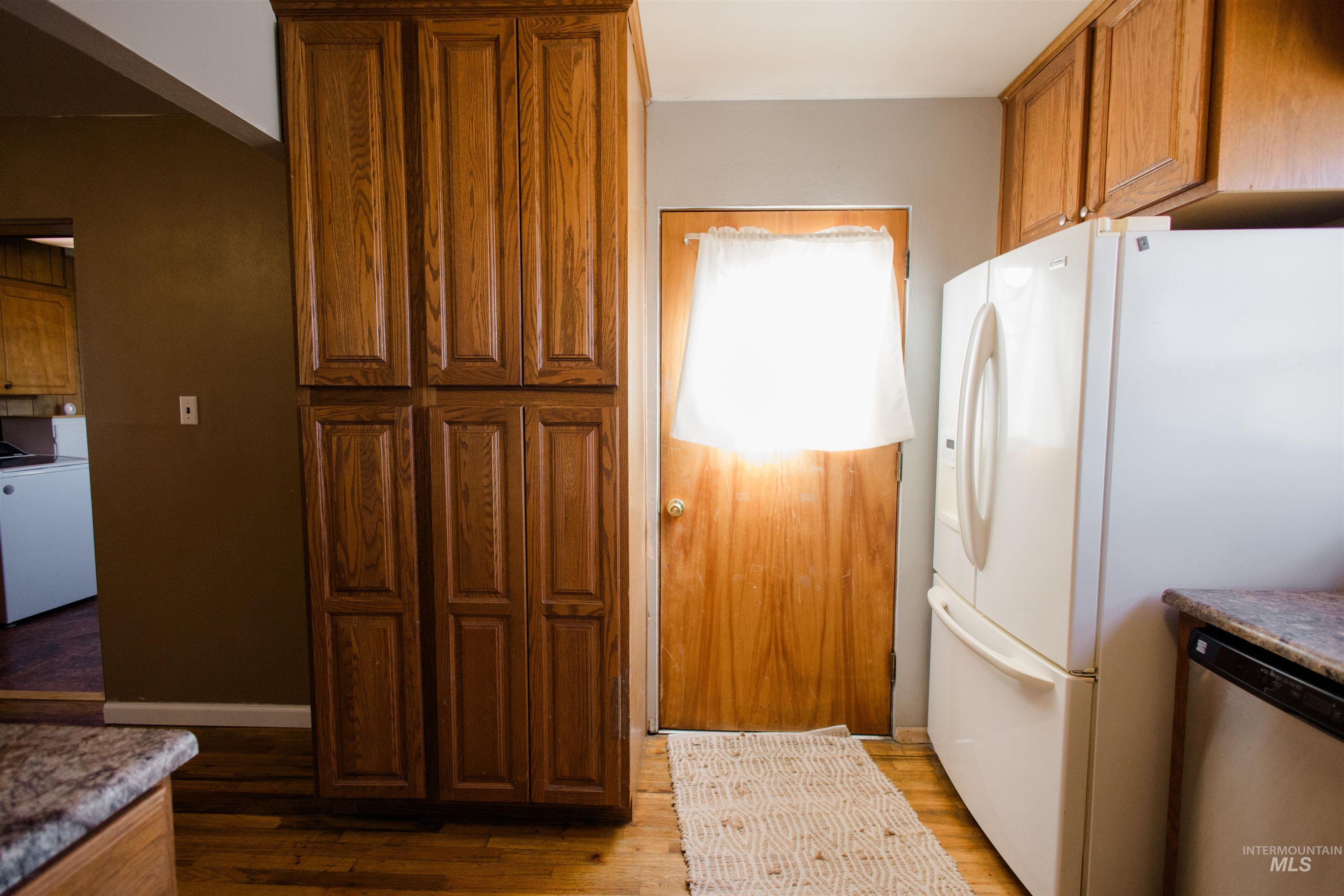 Kitchen featuring washer / clothes dryer, stainless steel dishwasher, brown cabinetry, white refrigerator with ice dispenser, and dark wood finished floors
