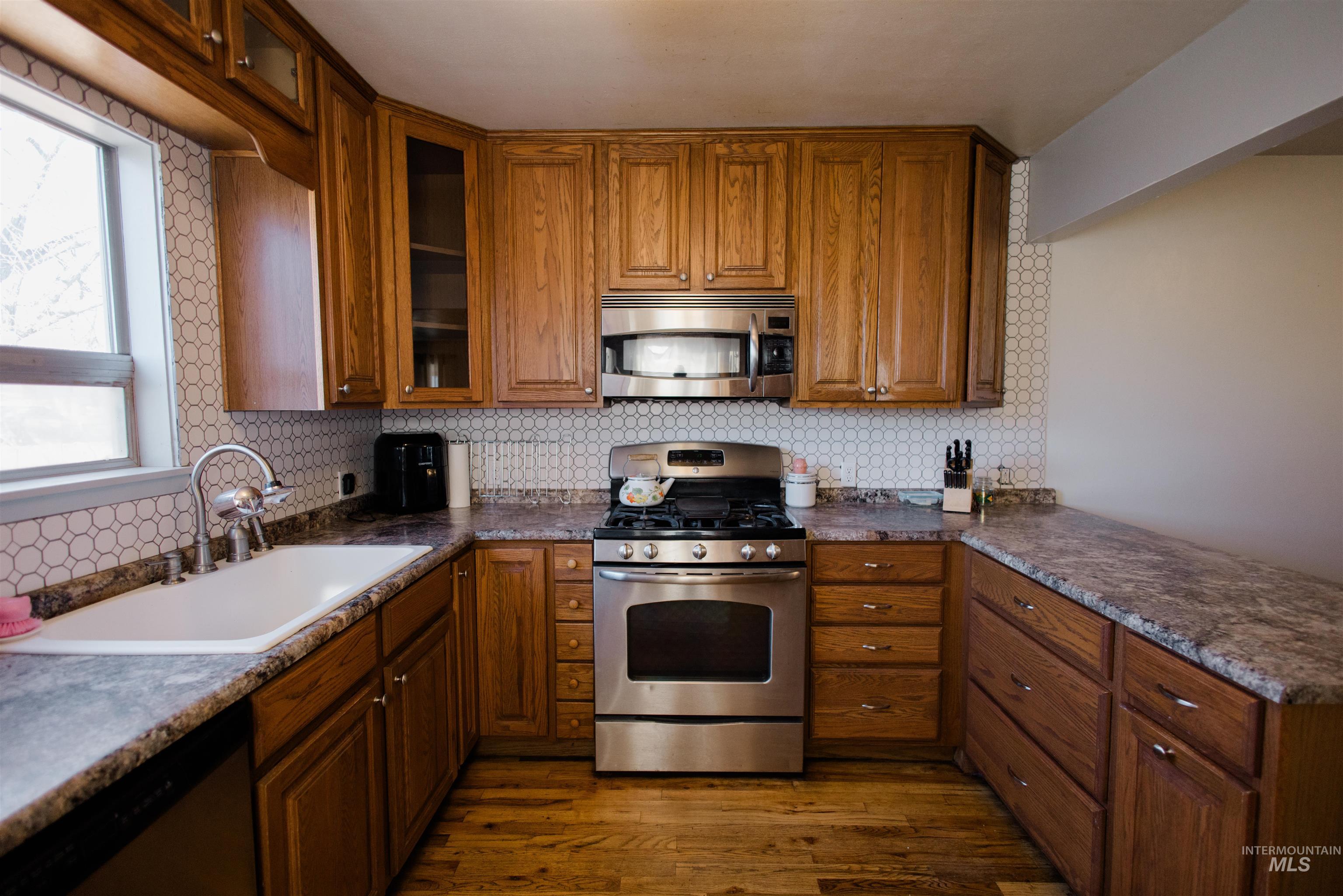 Kitchen with stainless steel appliances, brown cabinets, and dark wood-type flooring