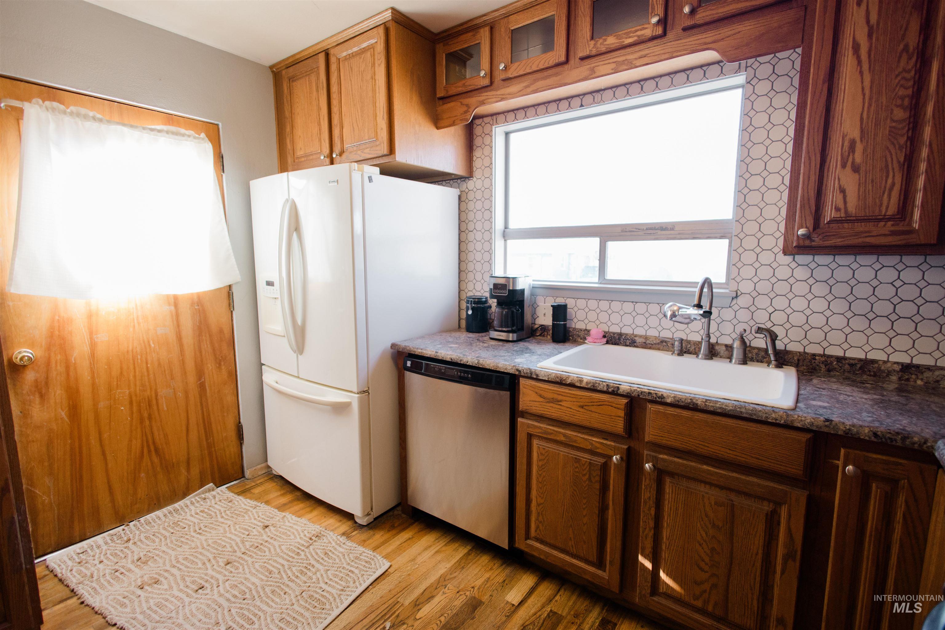 Kitchen featuring glass insert cabinets, dishwasher, brown cabinets, and light wood-style flooring