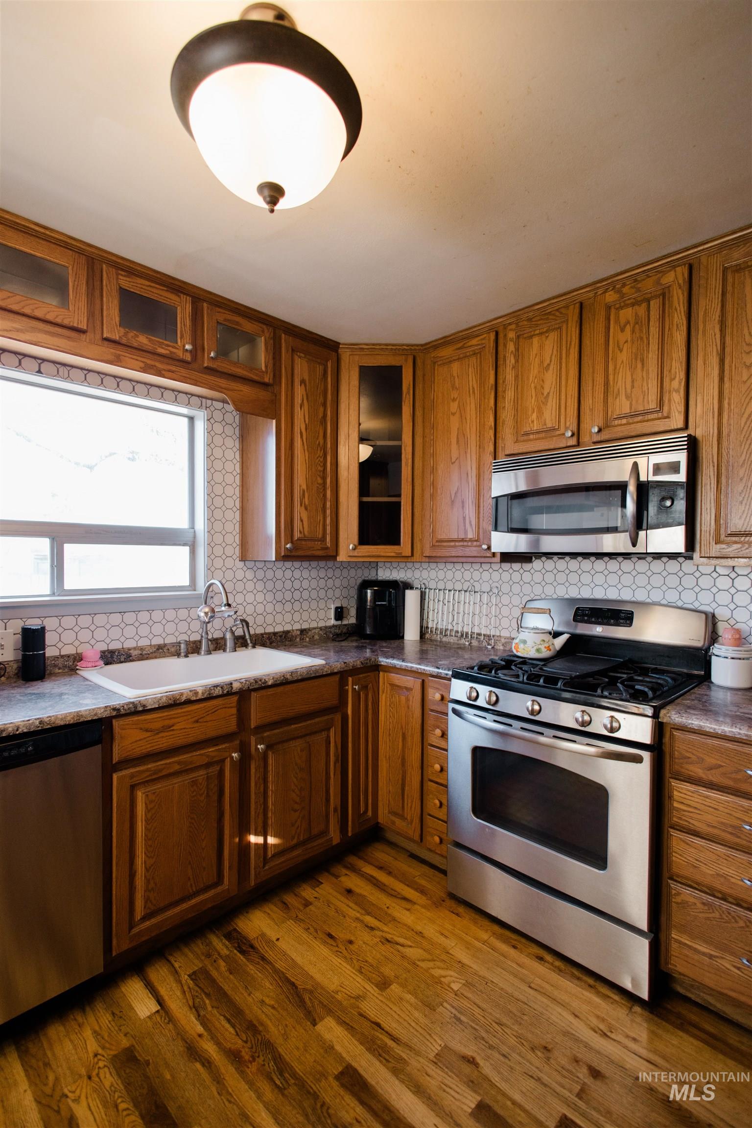 Kitchen featuring appliances with stainless steel finishes, brown cabinets, tasteful backsplash, and dark wood-type flooring