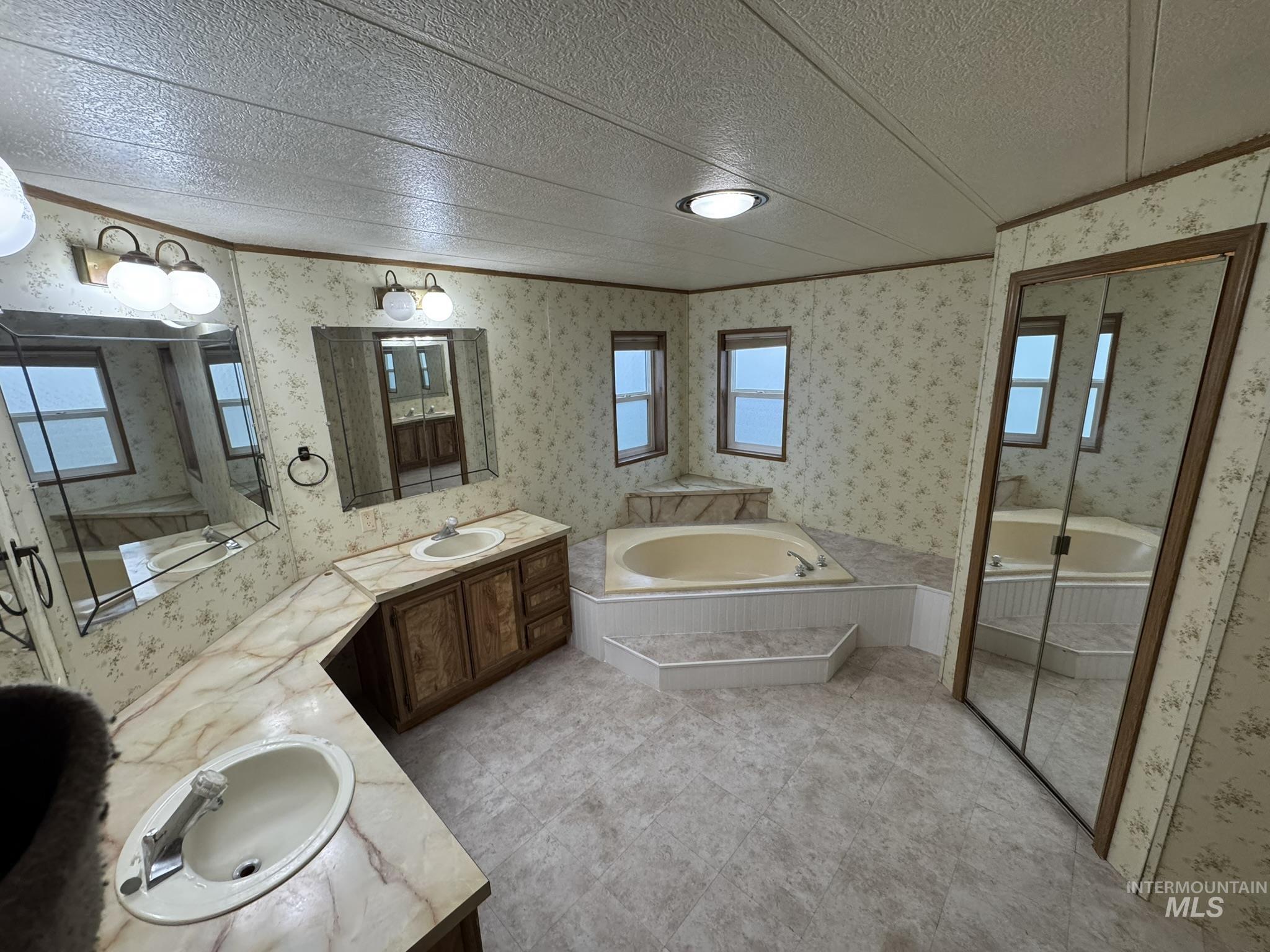 Full bathroom featuring plenty of natural light, double vanity, a bath, wallpapered walls, and a textured ceiling