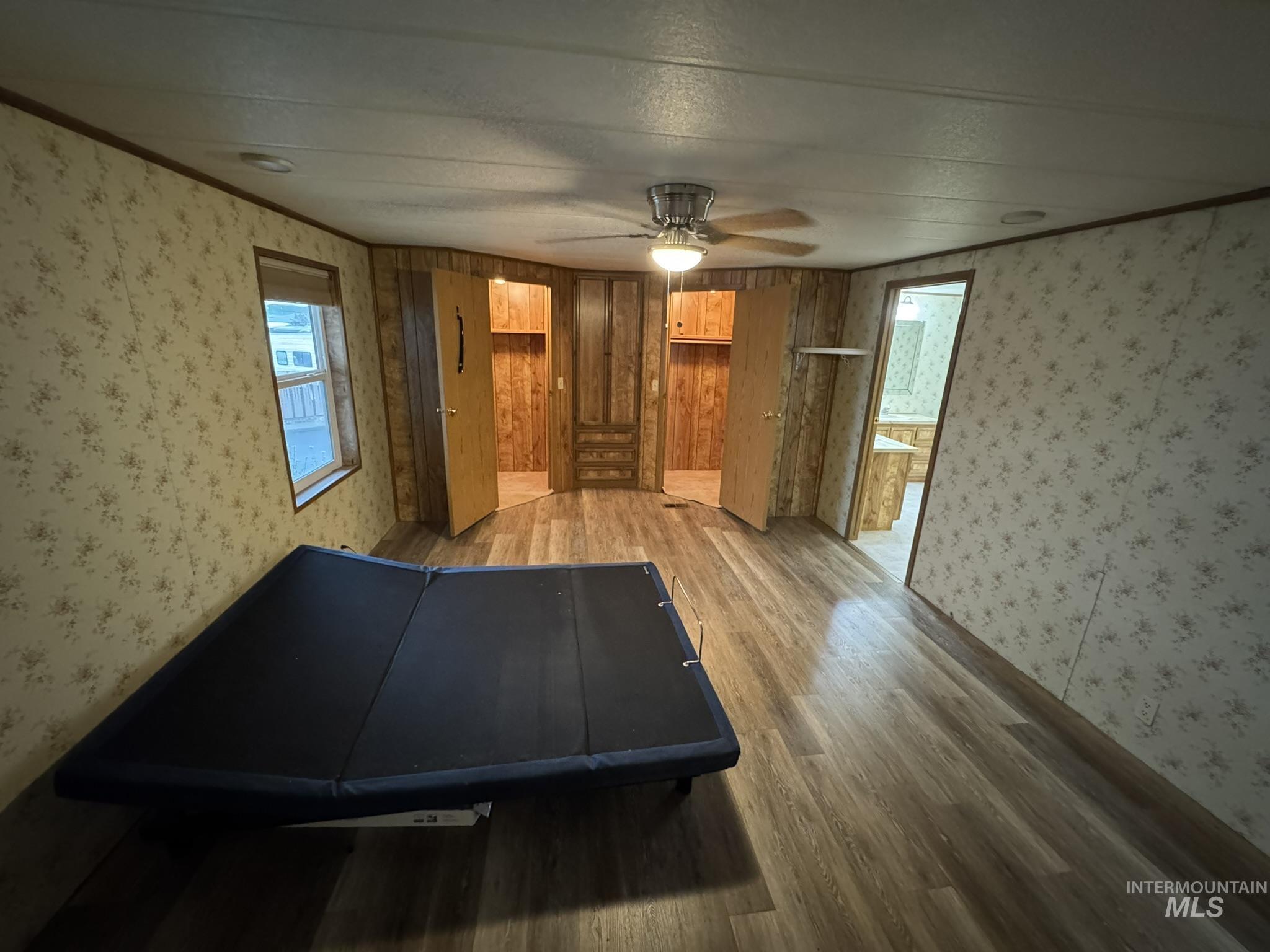 Unfurnished bedroom with wallpapered walls, wood finished floors, a ceiling fan, a closet, and ensuite bathroom