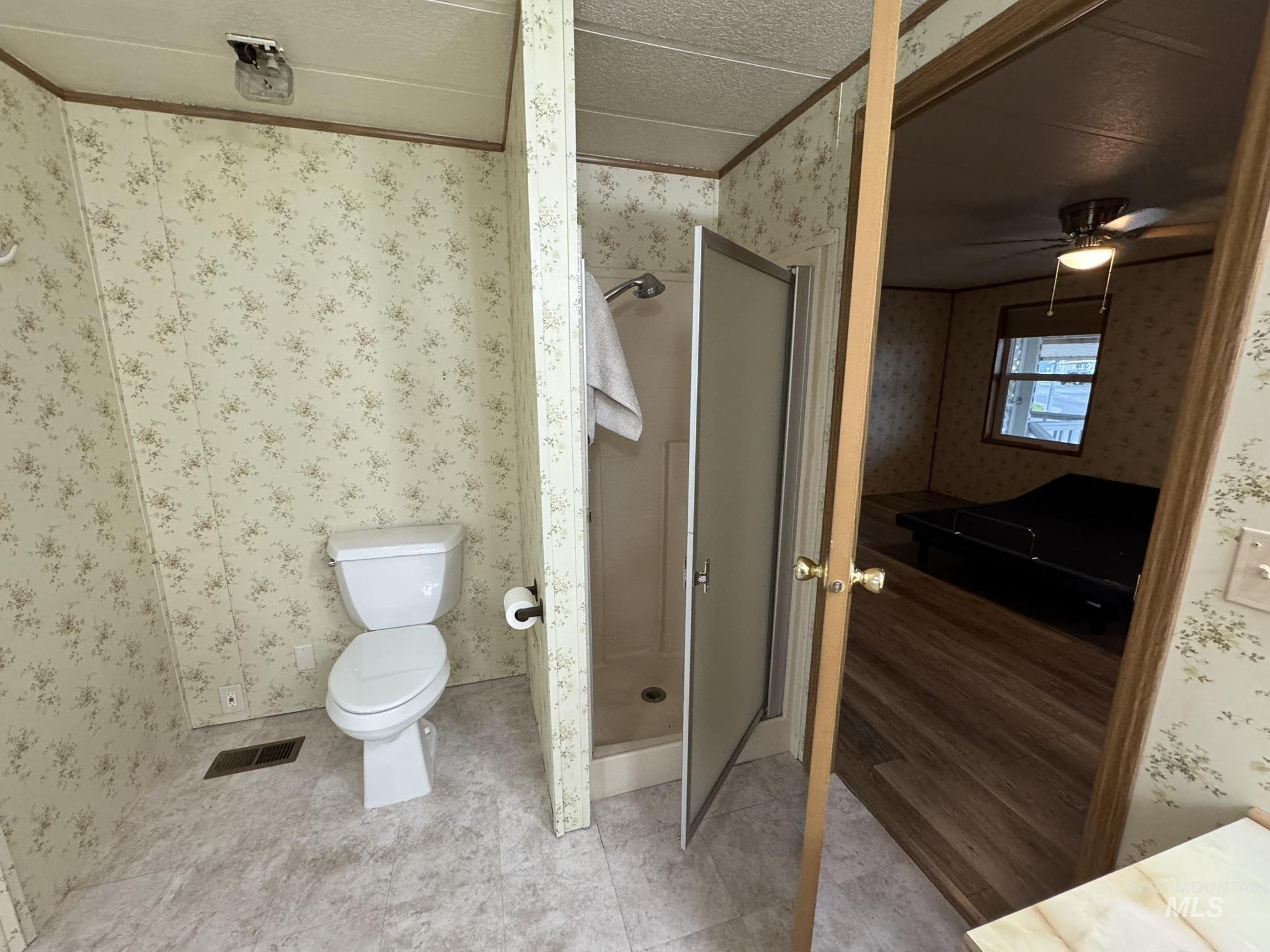 Full bathroom with a stall shower, wallpapered walls, and a ceiling fan