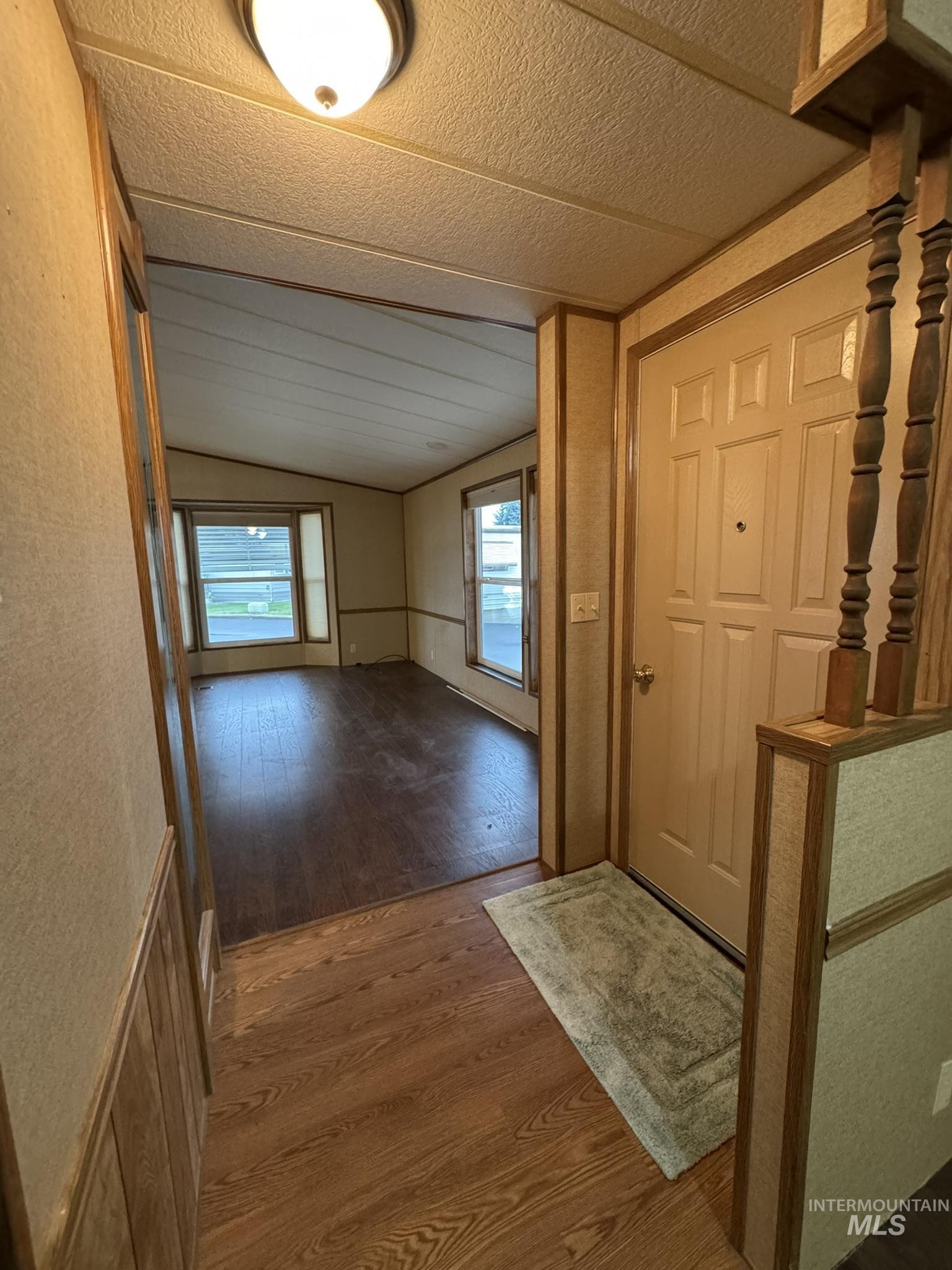 Entrance foyer with lofted ceiling, wood finished floors, and a textured wall
