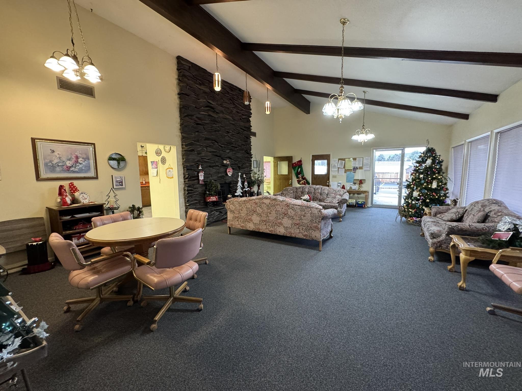Miscellaneous room featuring a chandelier, high vaulted ceiling, a stone fireplace, and beamed ceiling